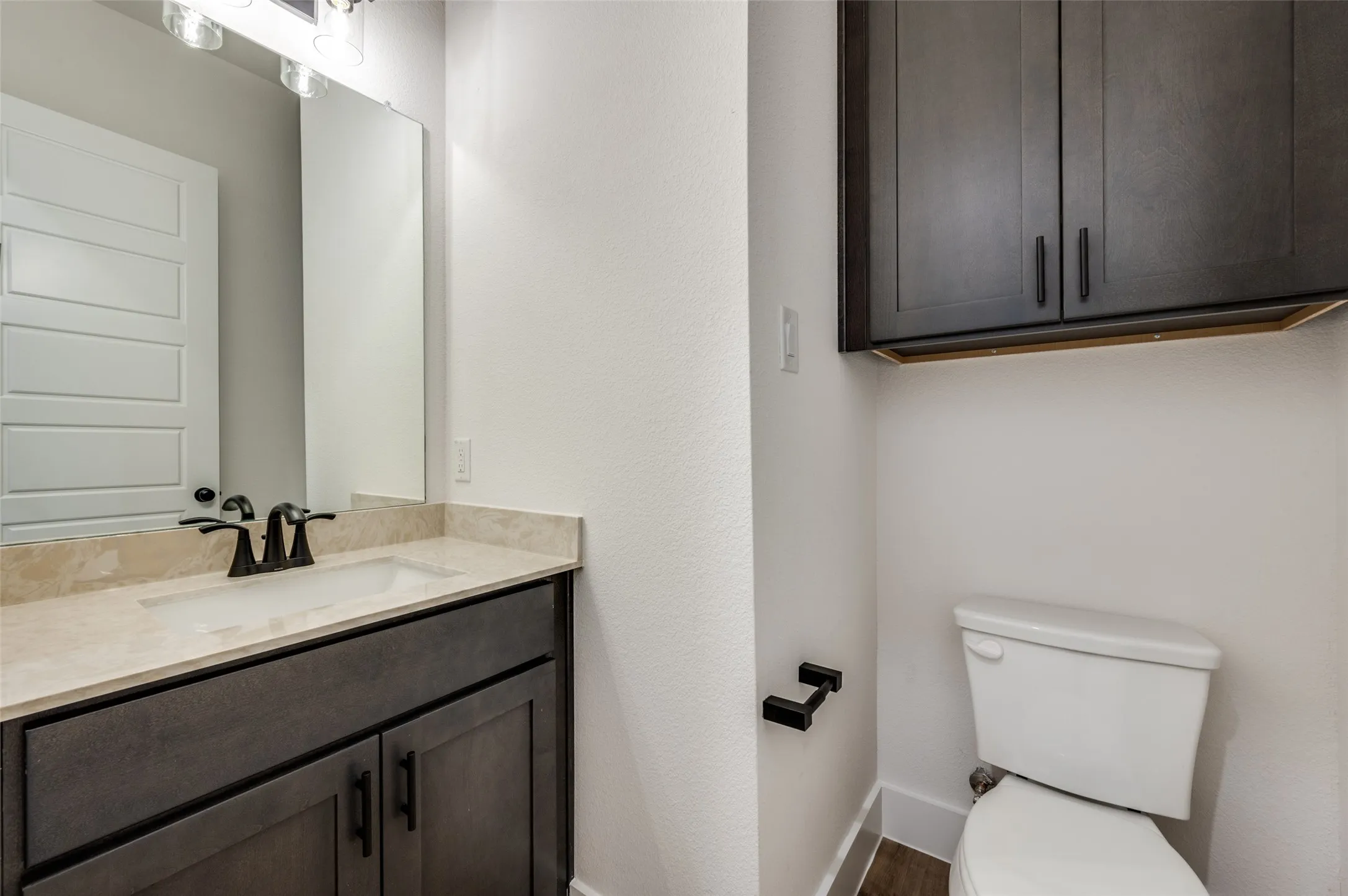 Chic and convenient half bath featuring a sleek vanity with generous counter space, modern black fixtures, and a large mirror. Additional built-in cabinetry provides valuable storage, making this stylish powder room both functional and perfect for guests.