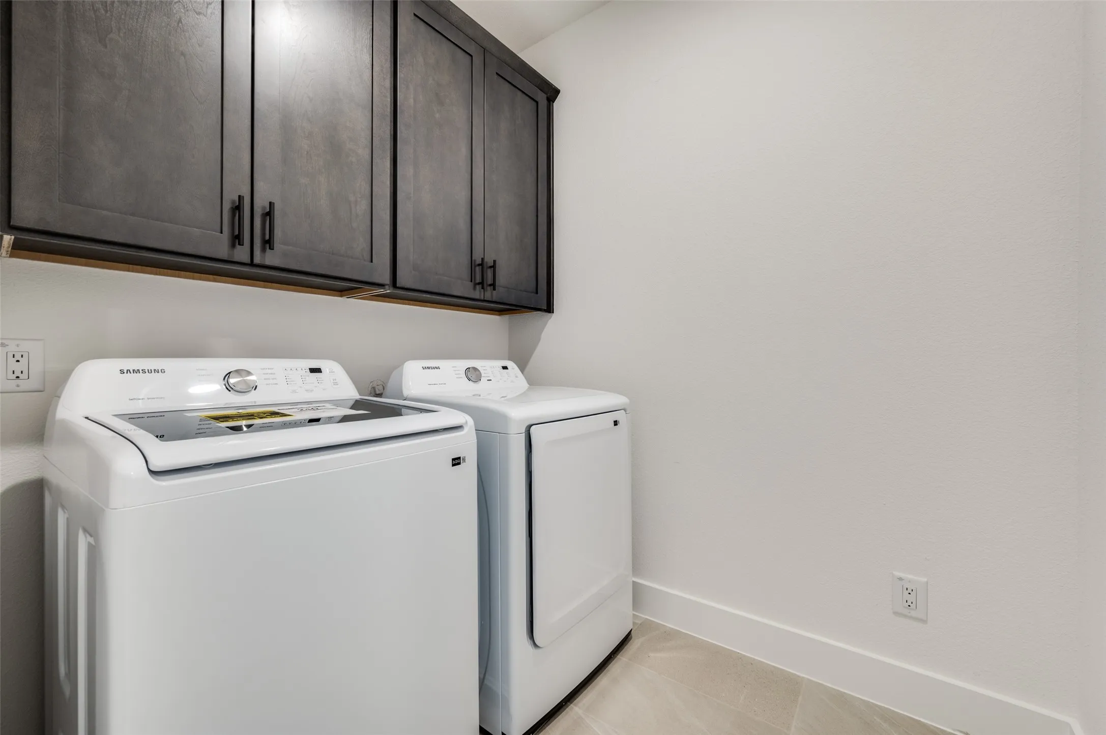 Spacious and functional laundry room featuring a full-size washer and dryer with abundant built-in cabinetry above for convenient storage. The generous layout provides additional space for organizing laundry essentials while keeping everything neatly tucked away.