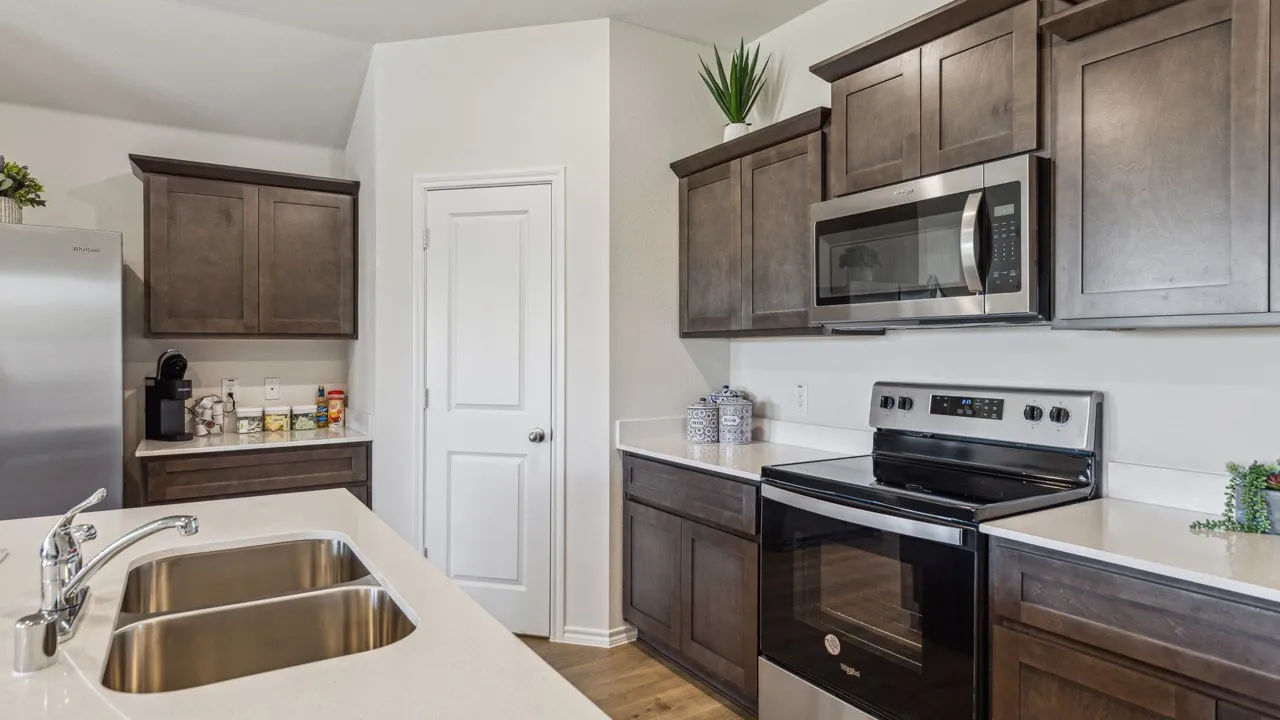 Kitchen featuring stainless steel appliances, dark wood finish cabinets, light wood finished floors, and light stone countertops