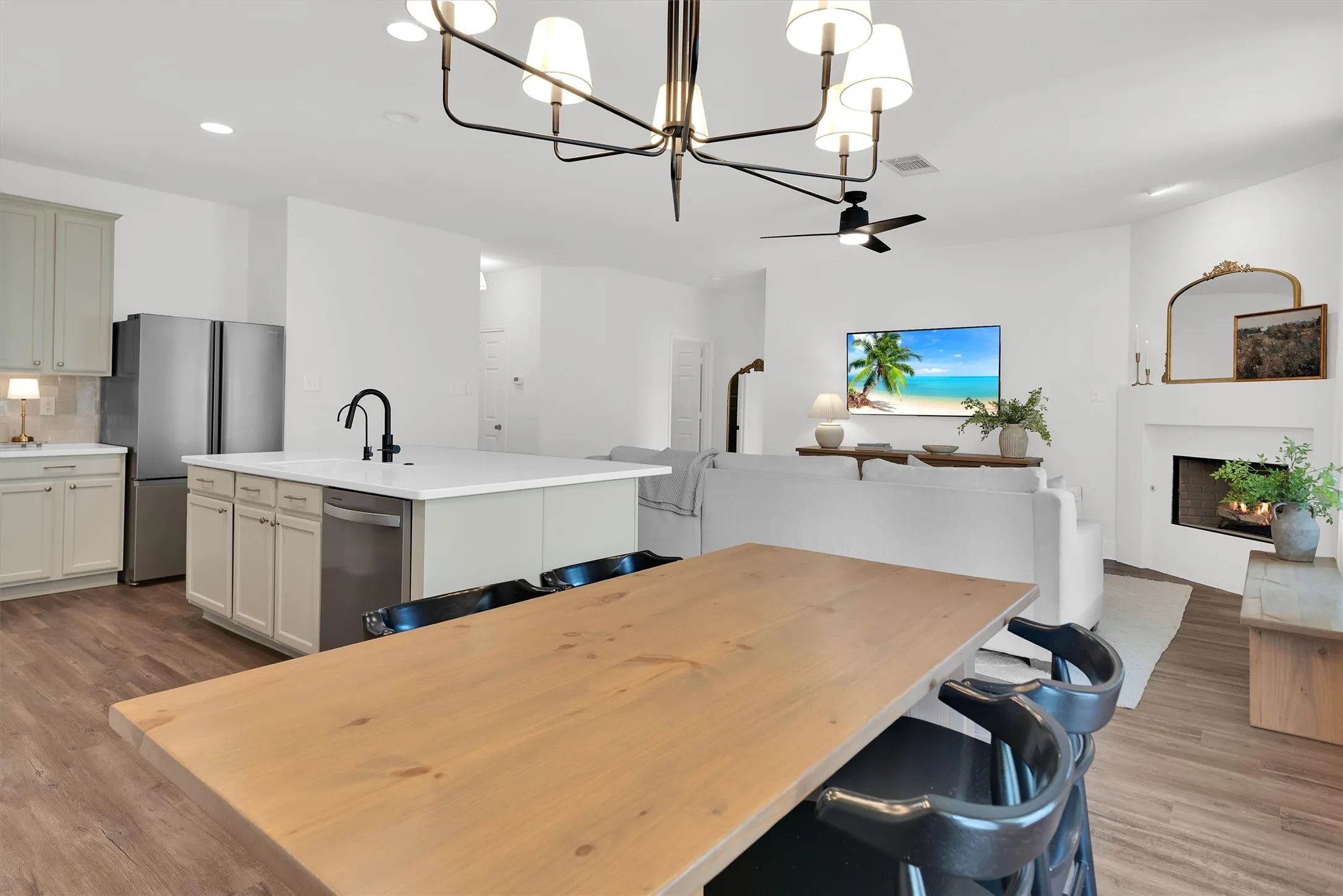 Open-concept living area featuring wood-finish flooring, a contemporary chandelier, and a white-painted fireplace