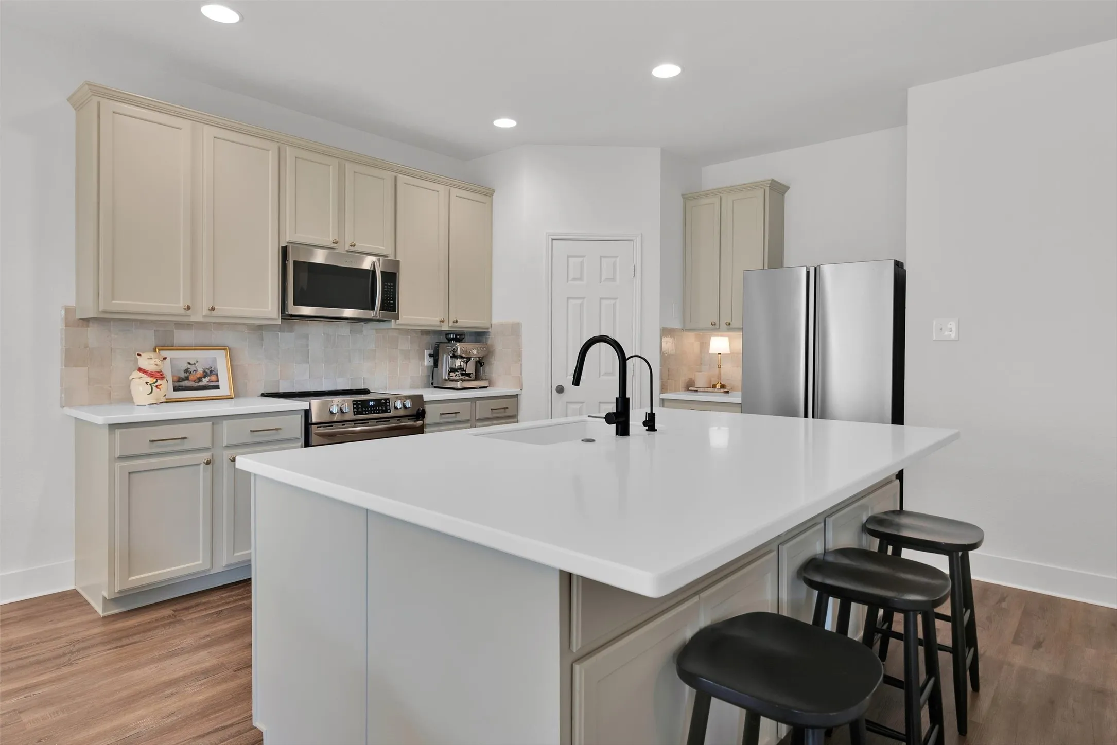 Kitchen featuring a center island, stainless steel appliances, light-toned cabinetry, a tile backsplash, and wood-finish flooring