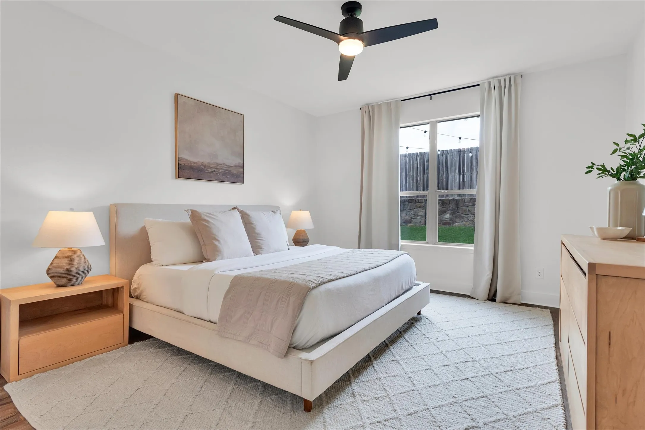 Spacious room featuring wood-finish flooring, a contemporary ceiling fan with integrated lighting, and a window with a backyard outlook