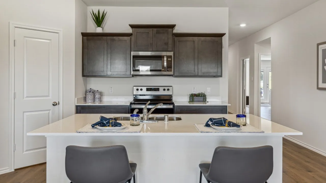 Kitchen with dark wood-style floors, dark wood finish cabinetry, stainless steel appliances, a kitchen island with sink, and light stone counters