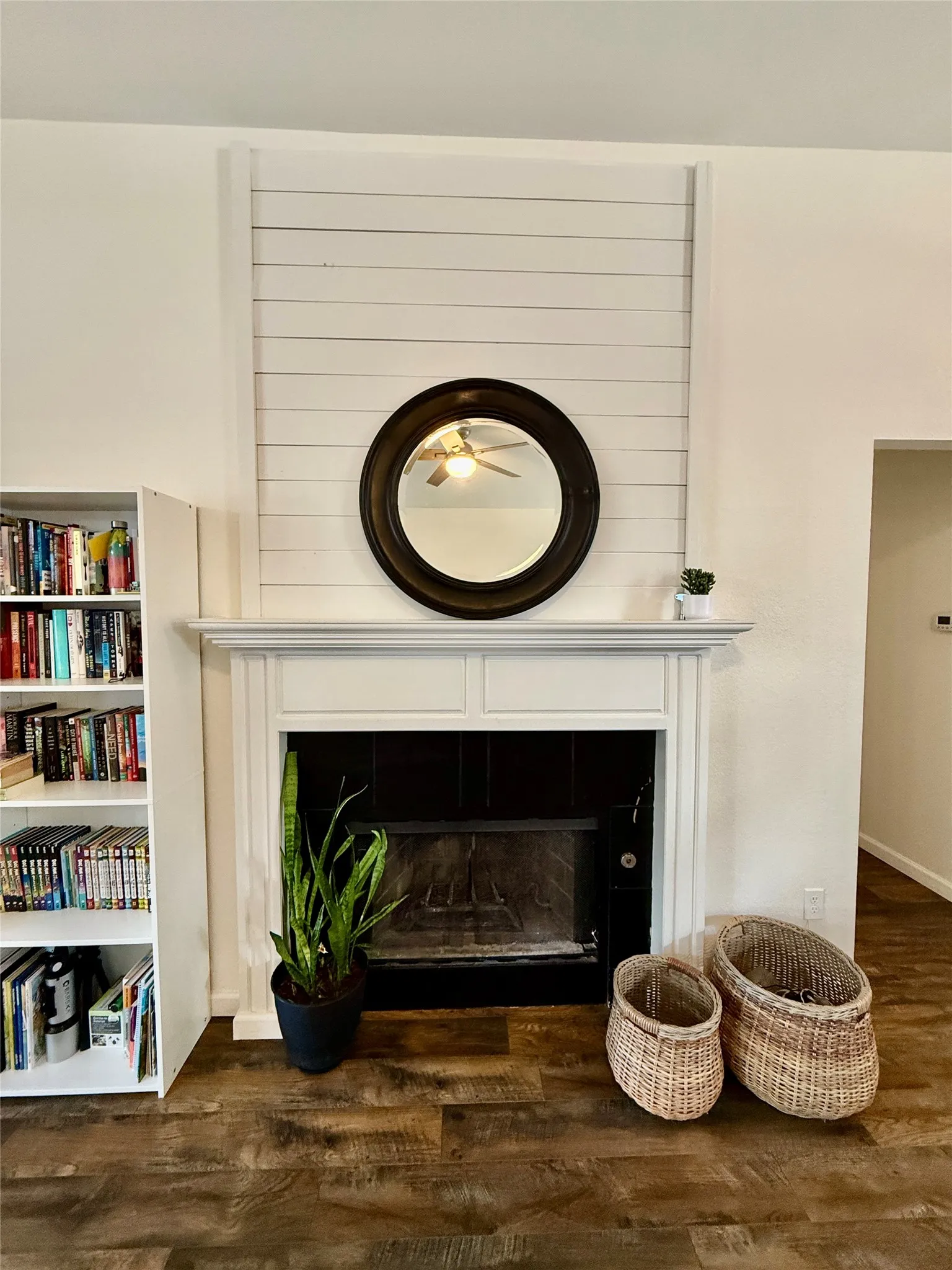 Fireplace with a shiplap-style surround, traditional white mantel, black firebox, and wood-finish flooring