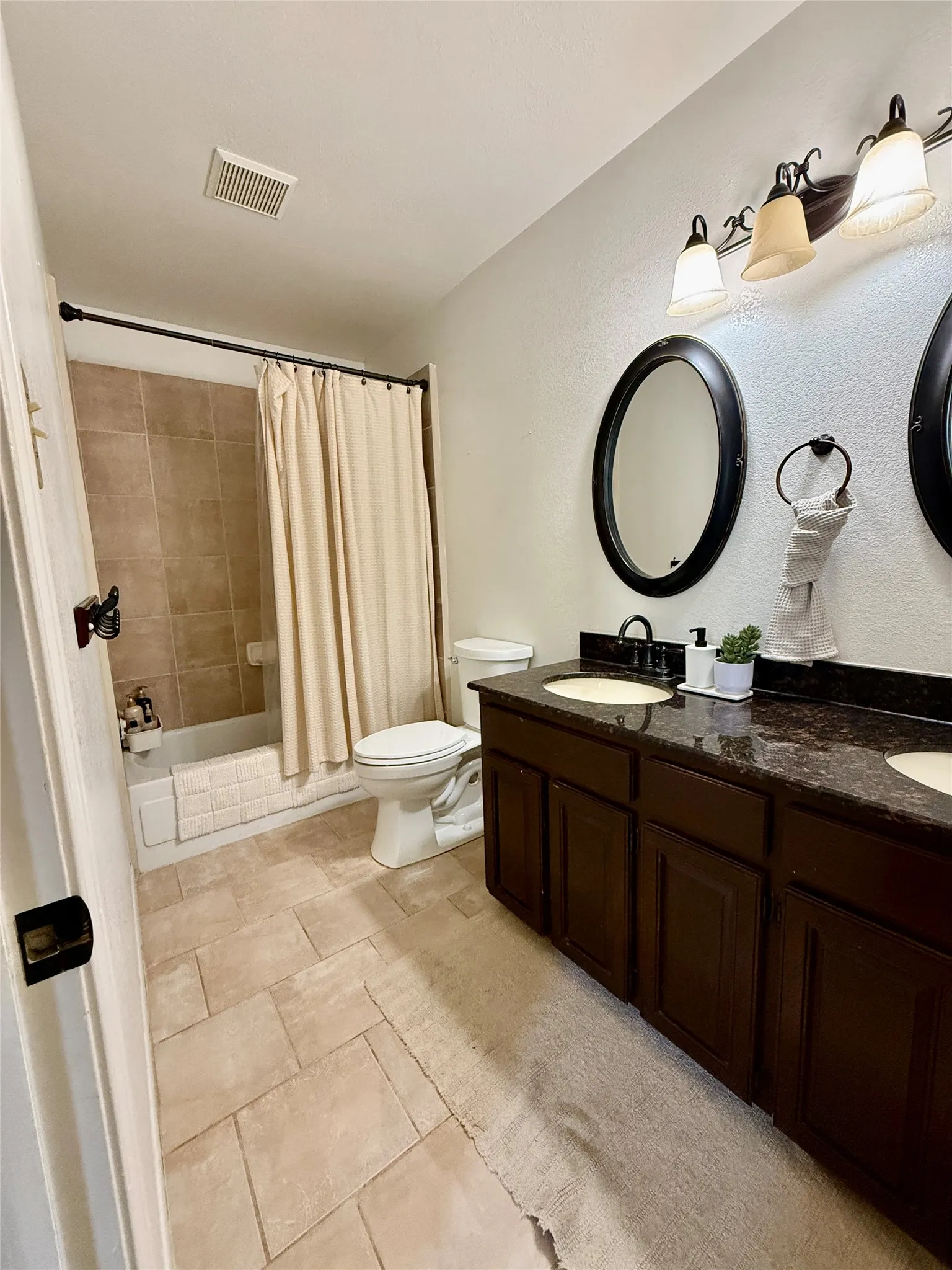Dual vanity with dark wood-finish cabinetry, countertop with integrated sinks, and individual oval mirrors