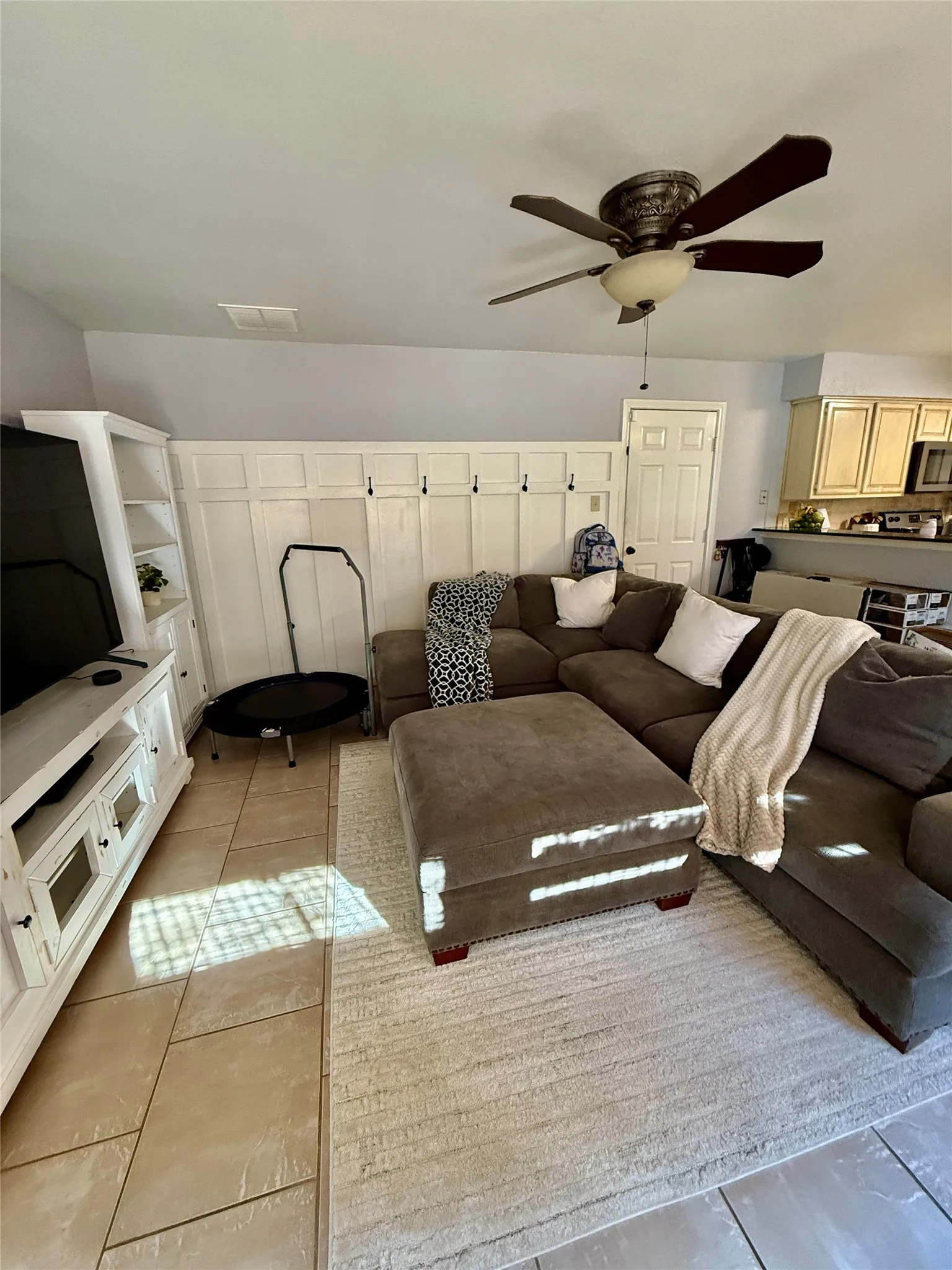 Tiled flooring, built-in shelving, paneled accent wall with hooks, and a ceiling fan with light fixture