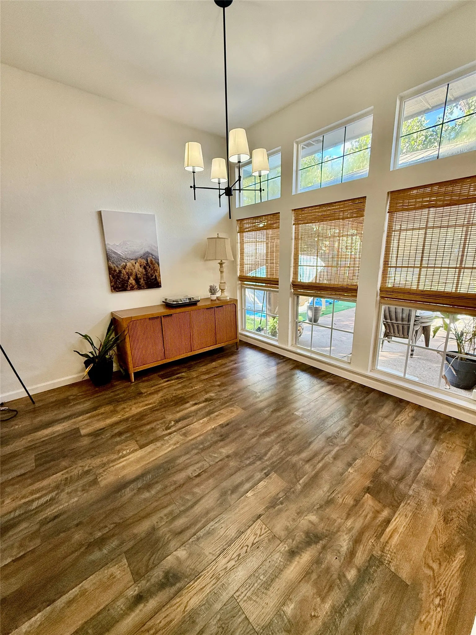 High ceilings with a modern chandelier, large windows, wood-finish flooring, and natural woven shades