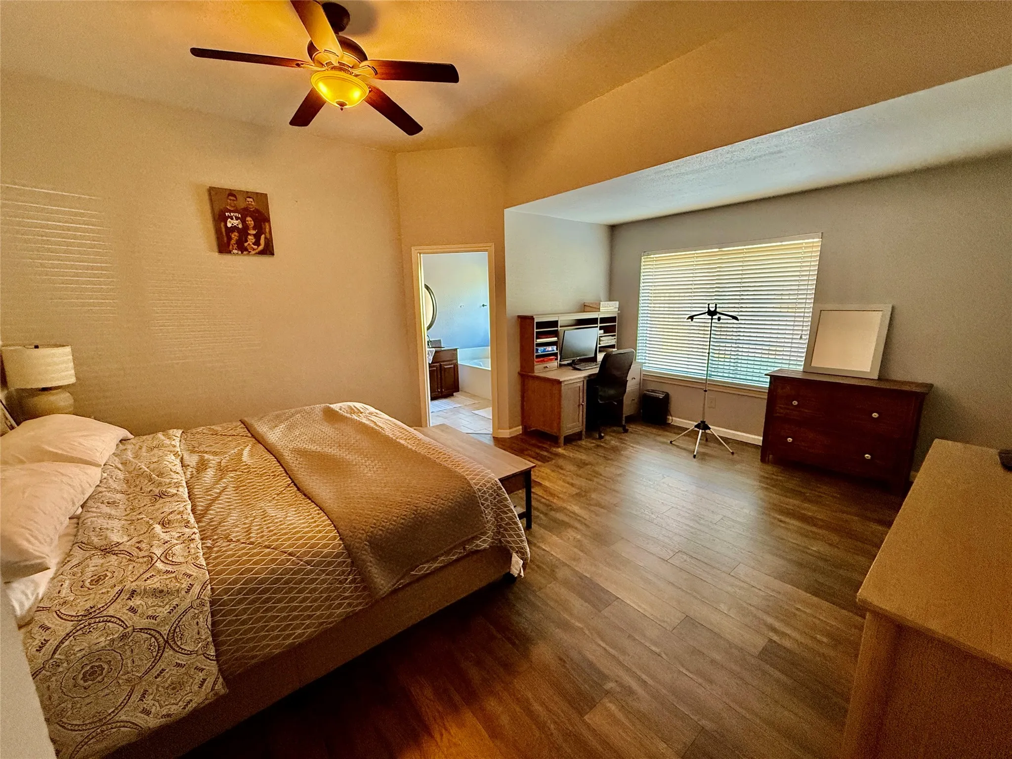 Recessed ceiling with wood-finish flooring, ceiling fan with integrated lighting, and multiple windows with blinds