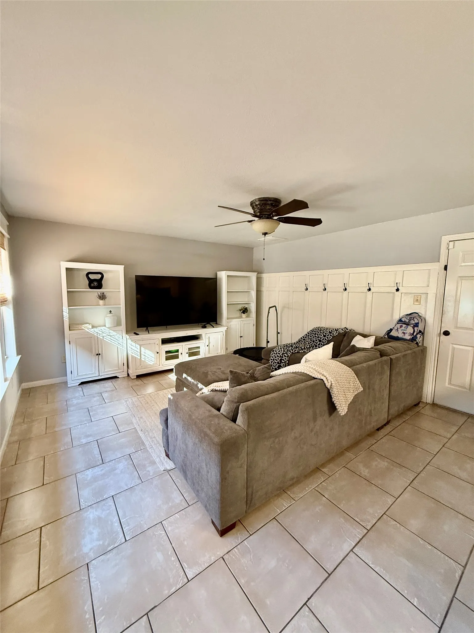 Vaulted ceiling, ceiling fan, tile flooring, built-in media console, architectural wall paneling