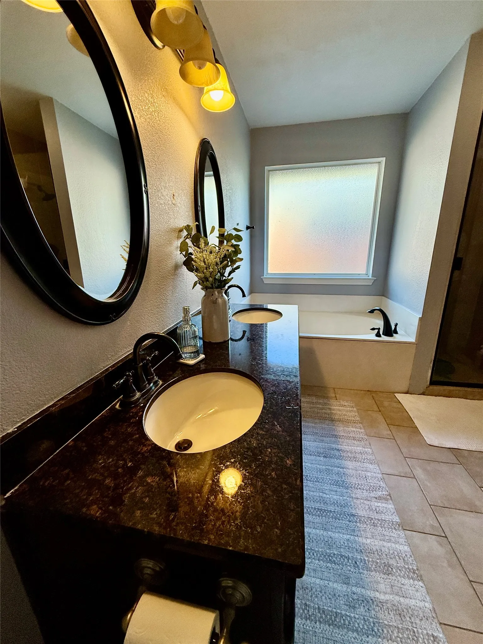 Dual vanity with dark stone countertop, integrated sinks, and dark-finished fixtures