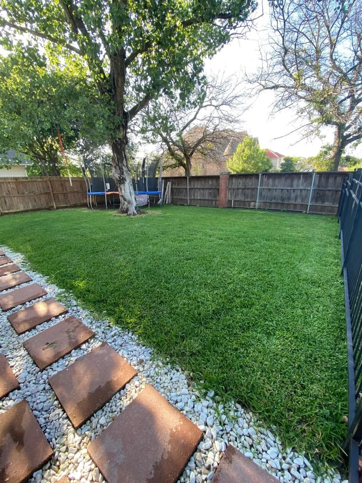Expansive backyard featuring a lush lawn, stepping stone path with gravel, and mature trees