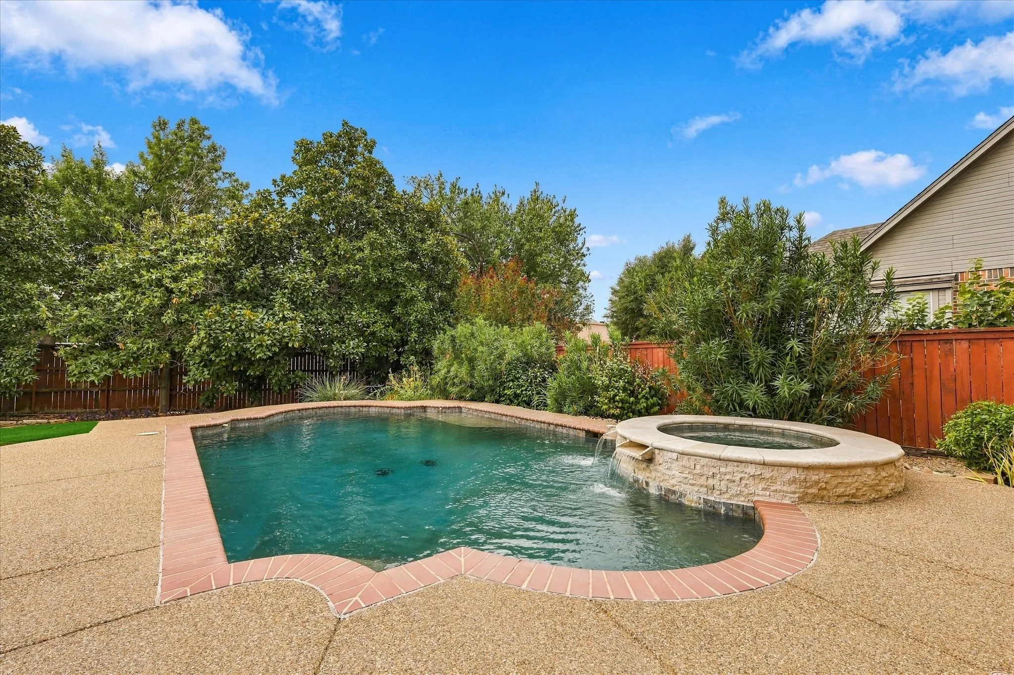 Swimming pool with brick coping, an integrated spa with stone-finish surround, and a surrounding aggregate concrete patio