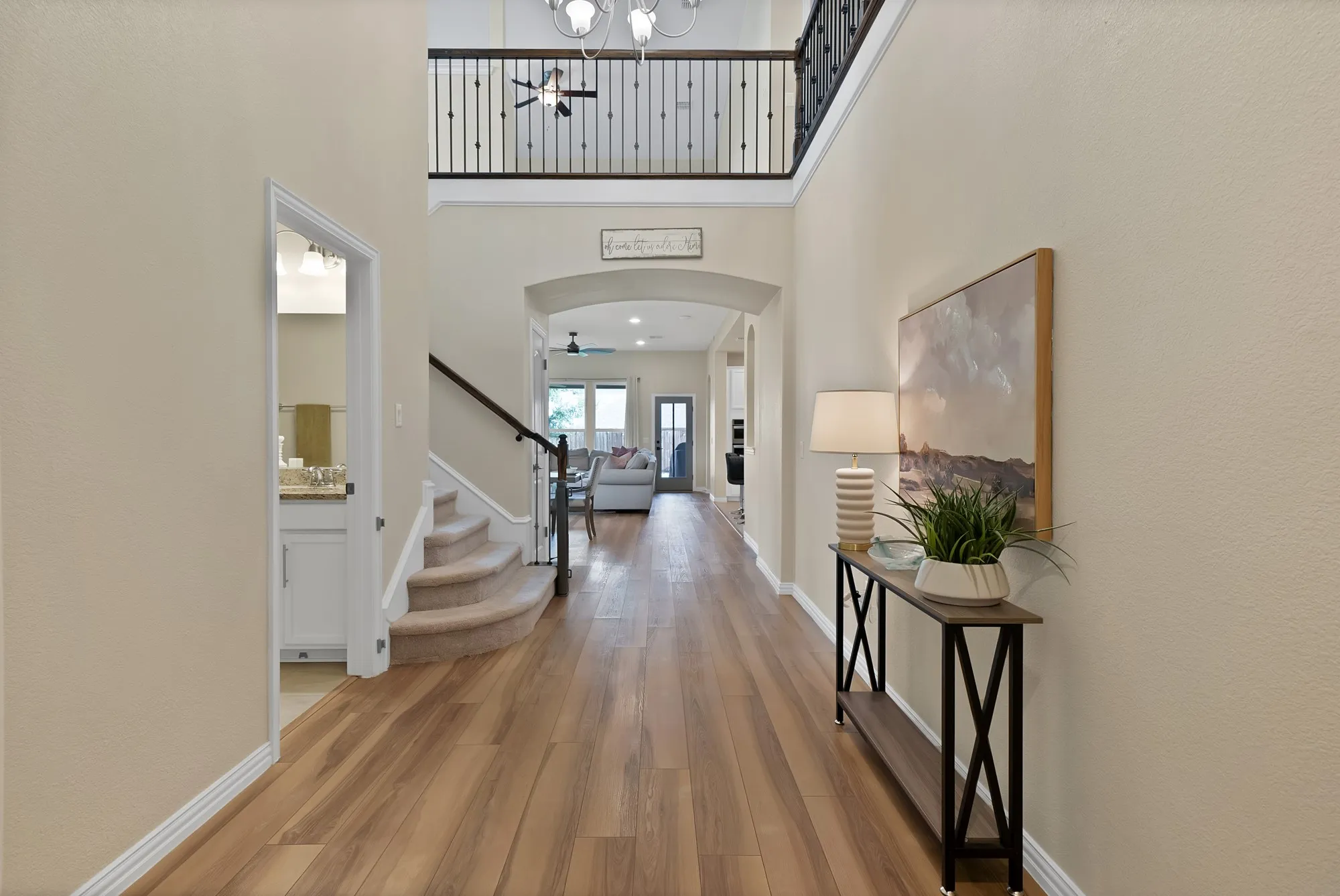 Two-story foyer with wood-finish flooring, staircase featuring carpeting and dark wood railing, and an arched entry