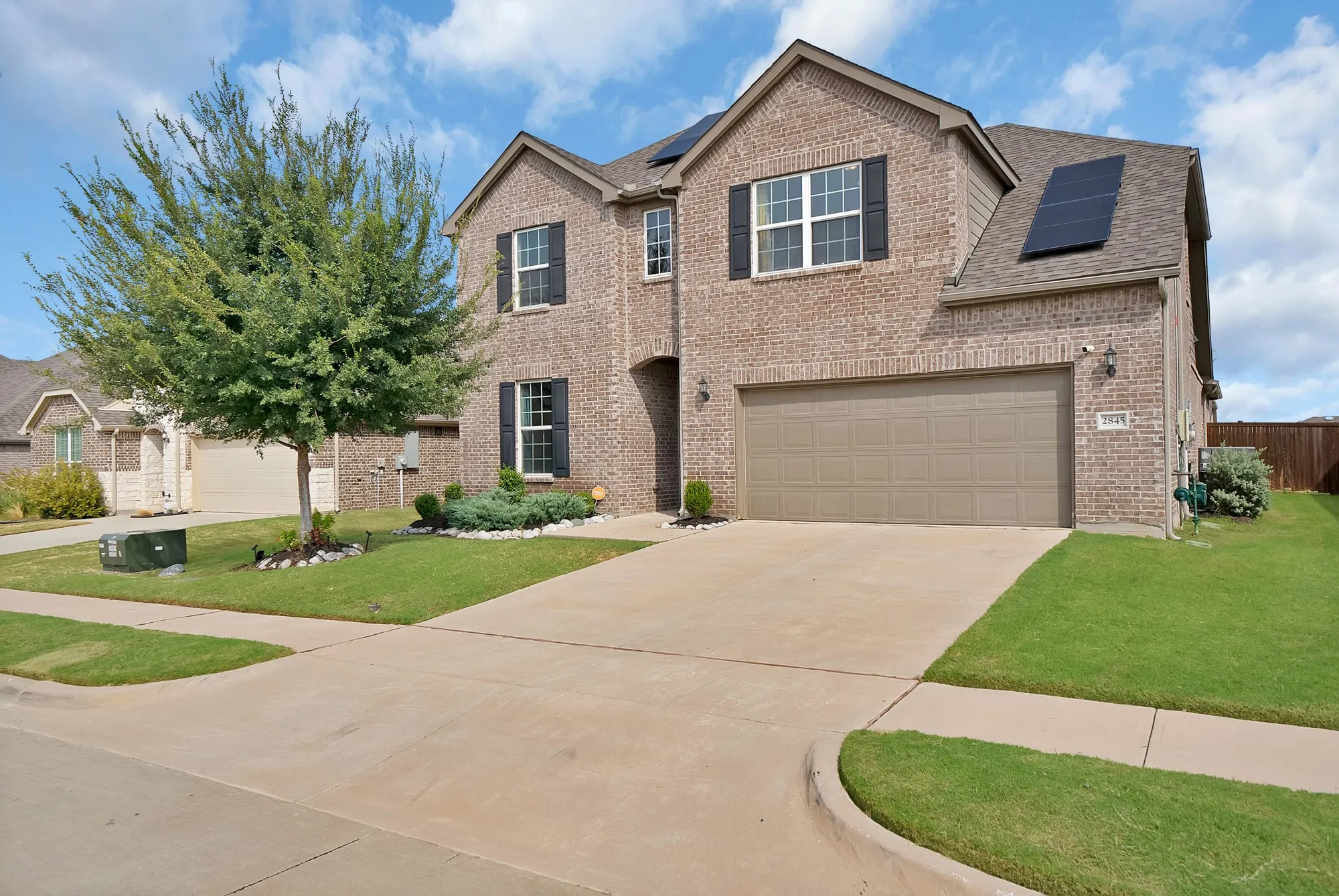 Brick exterior with a two-car garage, mature landscaping, and solar panels