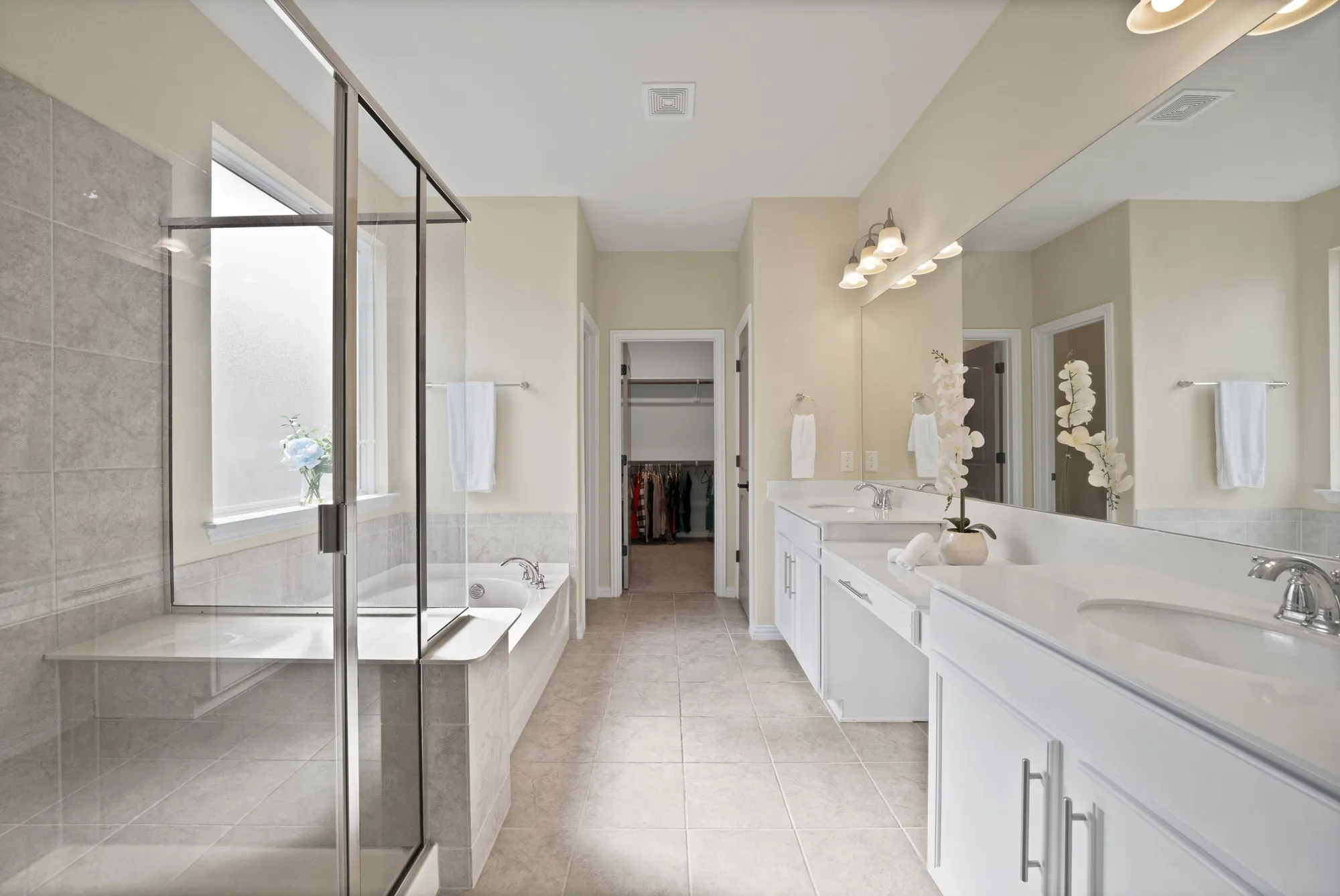 Spa-inspired primary bathroom featuring dual vanities with white cabinetry and brushed nickel hardware, ceramic vessel sinks, frameless glass-enclosed shower with tile surround, soaking tub, and neutral tile flooring throughout