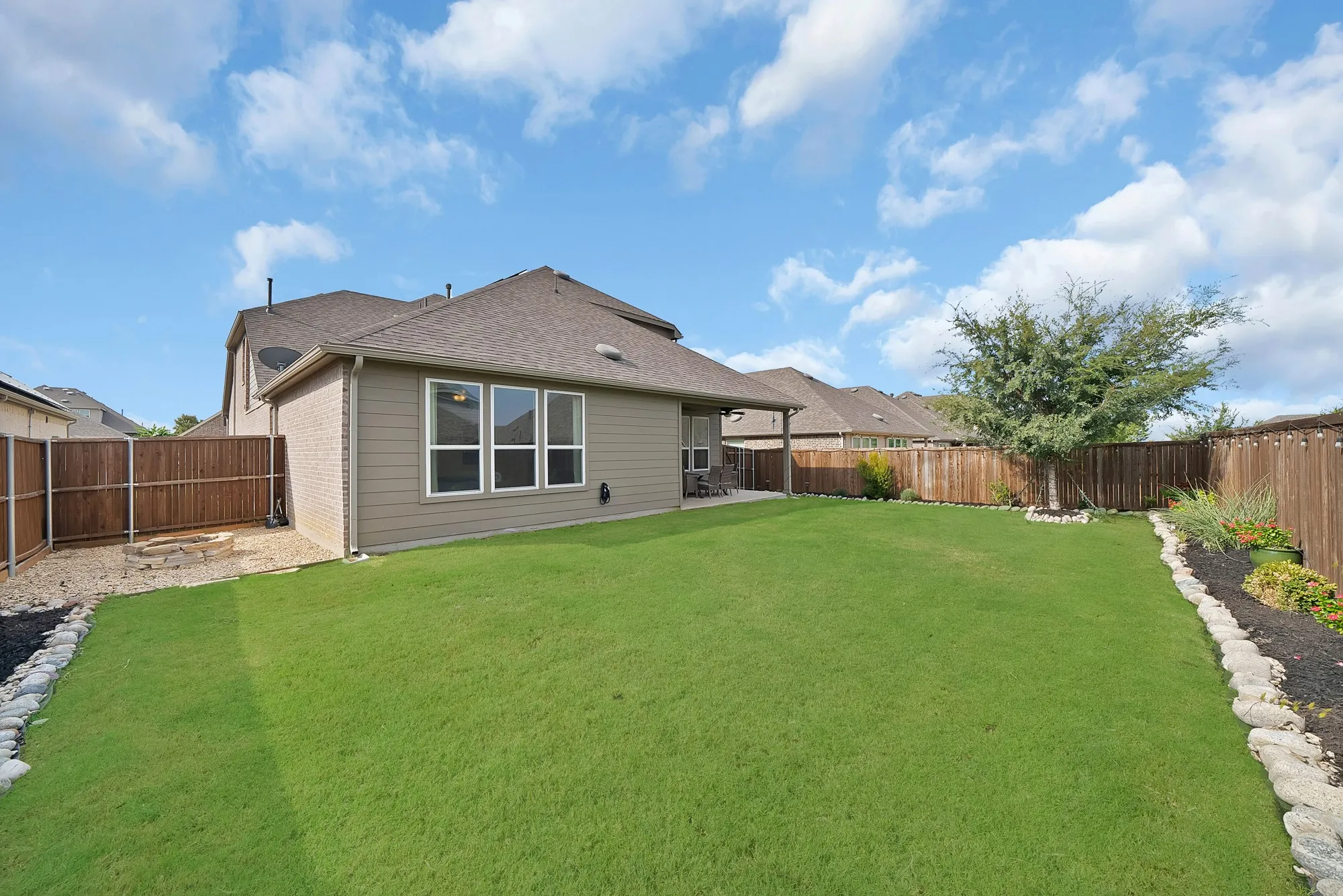 Expansive backyard with a manicured lawn, established tree, and a built-in fire pit area