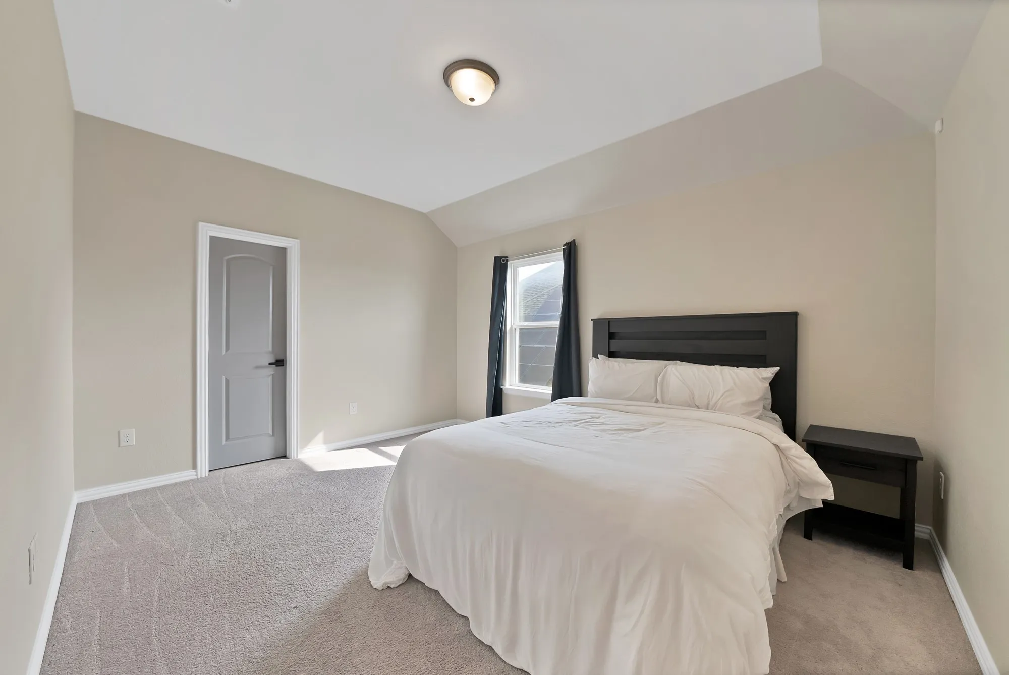 Vaulted ceiling, neutral wall paint, light gray carpeting, single window, and a gray interior door