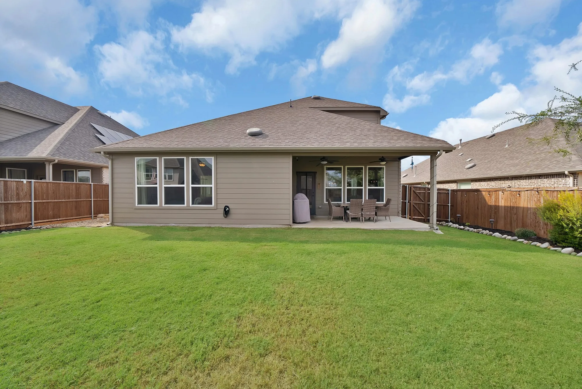 Expansive green lawn with a covered patio, privacy fencing, and exterior wall lighting