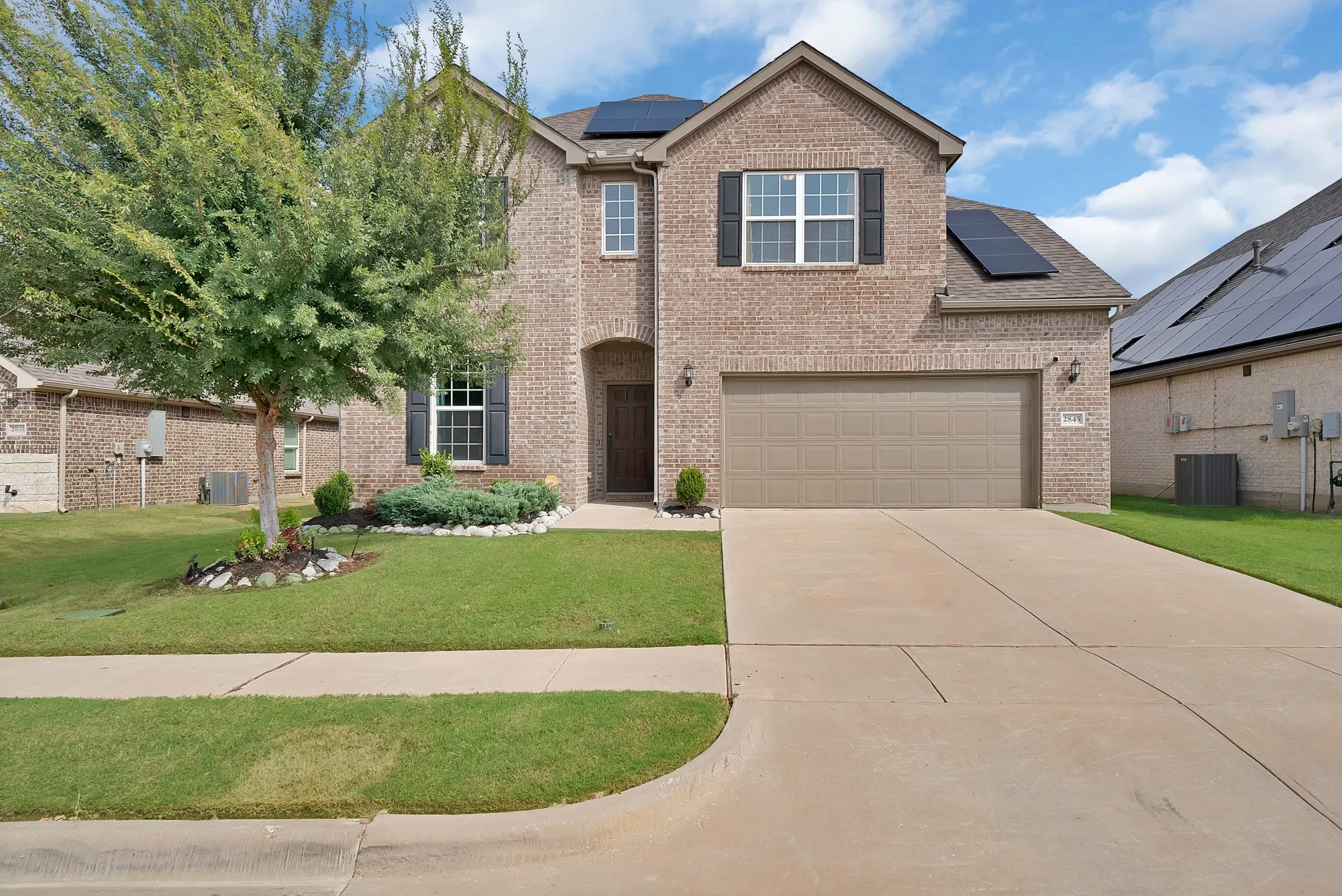 Brick facade, attached garage, concrete driveway, front lawn, and mature trees
