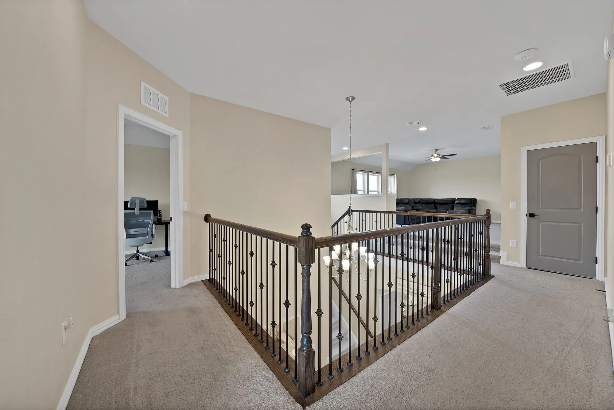 Spacious upper-level landing featuring dark wood-finish railings, neutral carpet flooring, and abundant natural light from multiple windows and ceiling fixtures