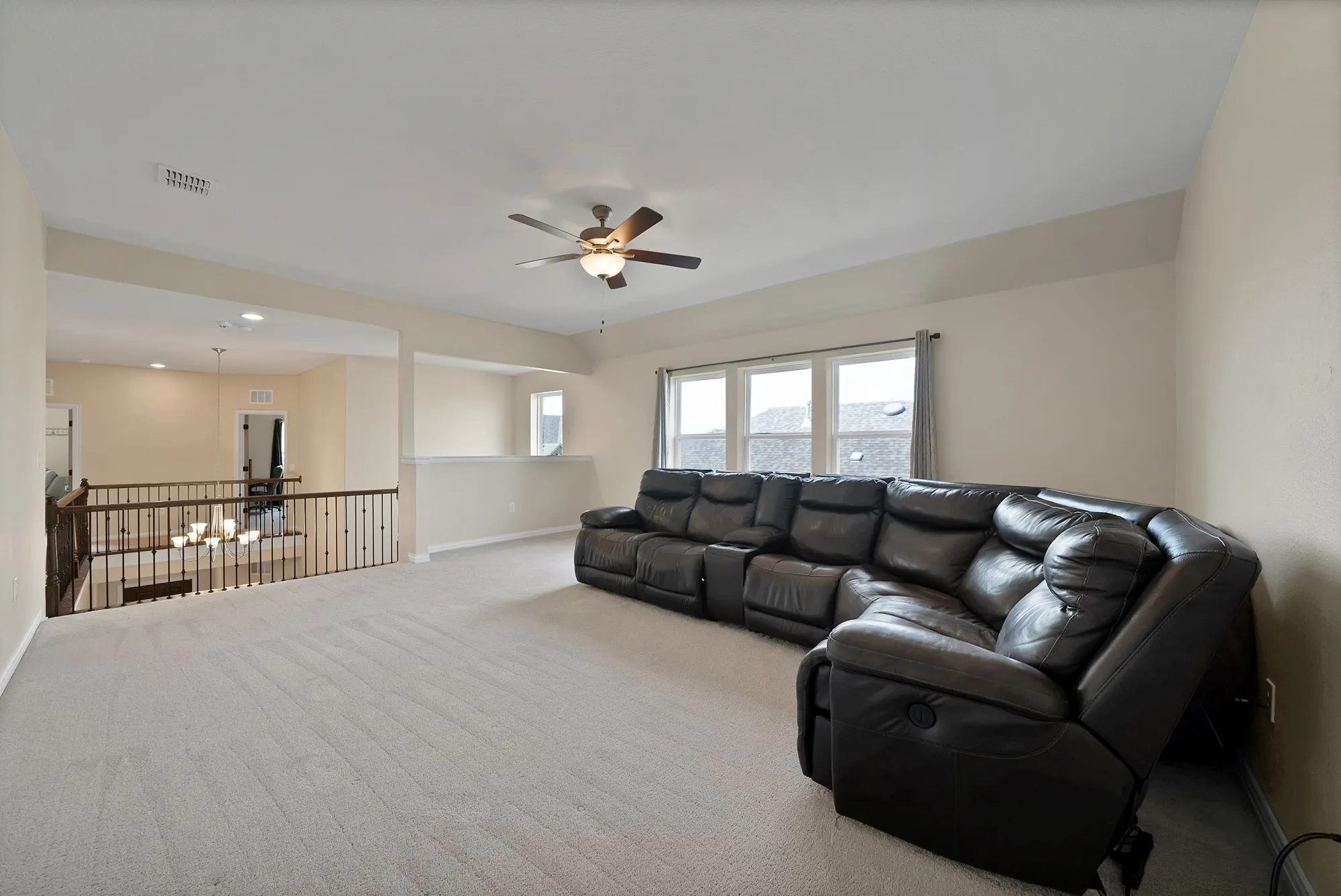 Spacious carpeted loft with an open railing overlooking the area below, featuring multiple windows and a ceiling fan