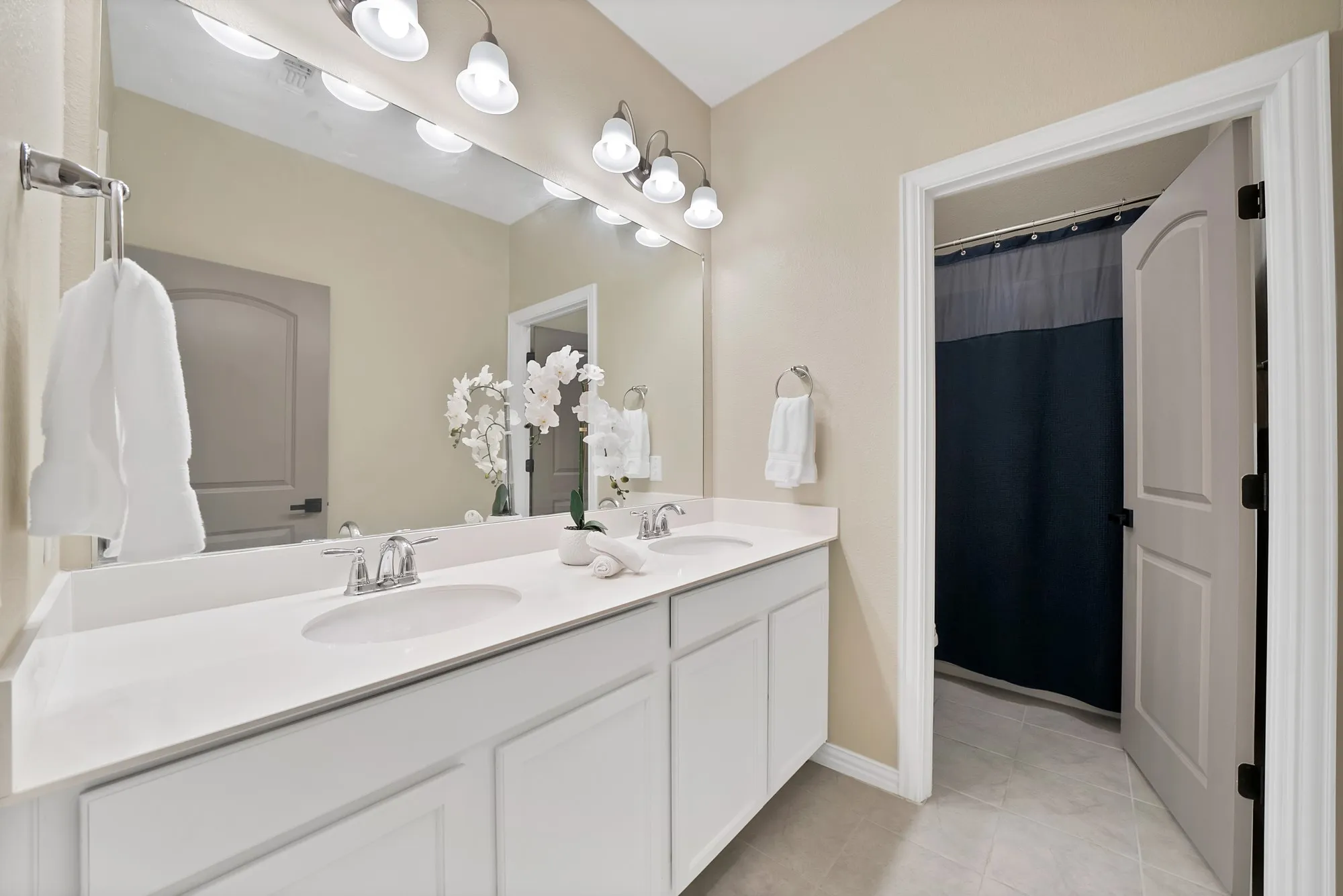 Dual vanity with integrated sinks, chrome fixtures, a full-width mirror, and overhead sconce lighting