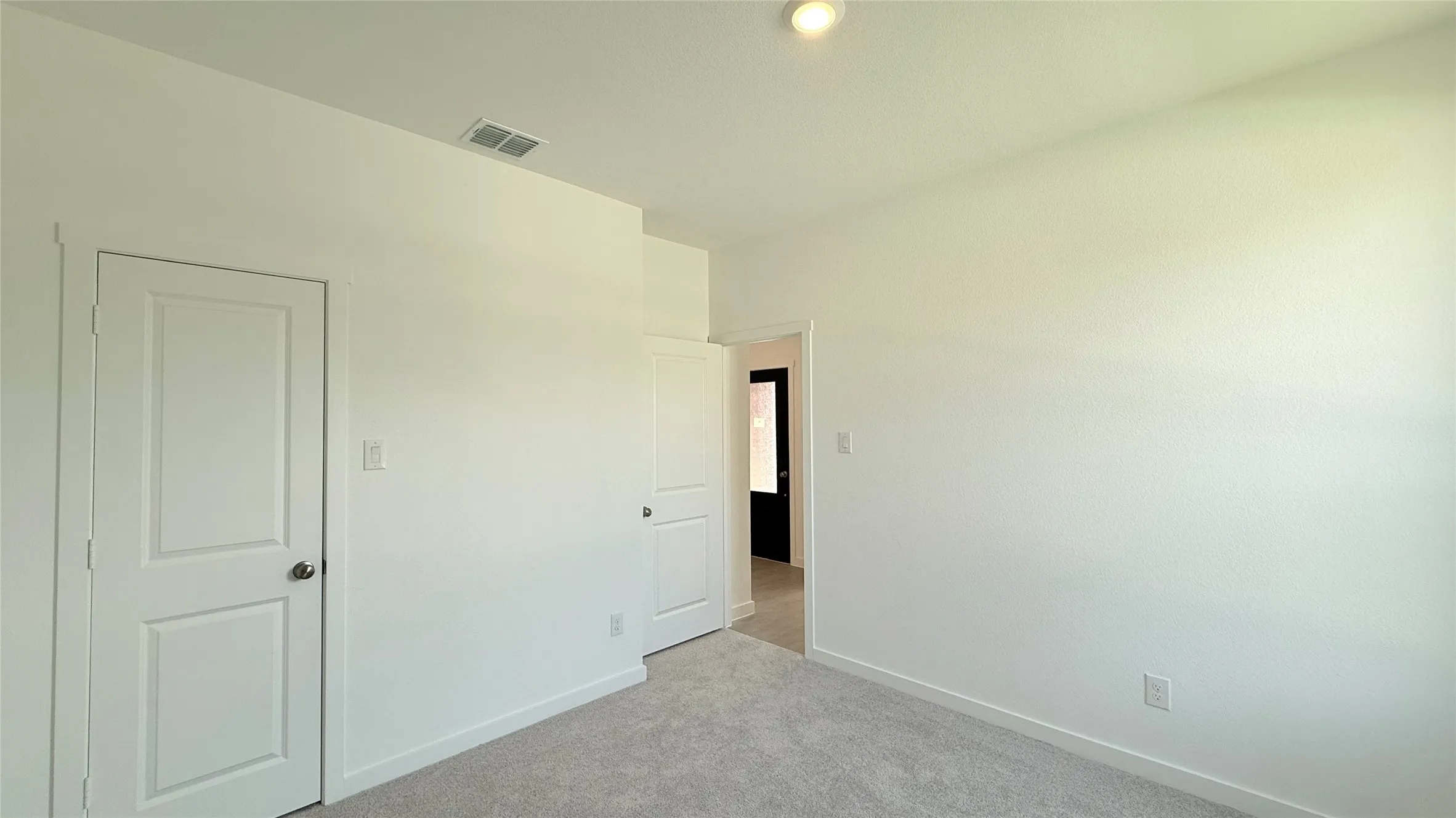 Recessed lighting illuminates the space, featuring white painted walls and light-toned carpeting