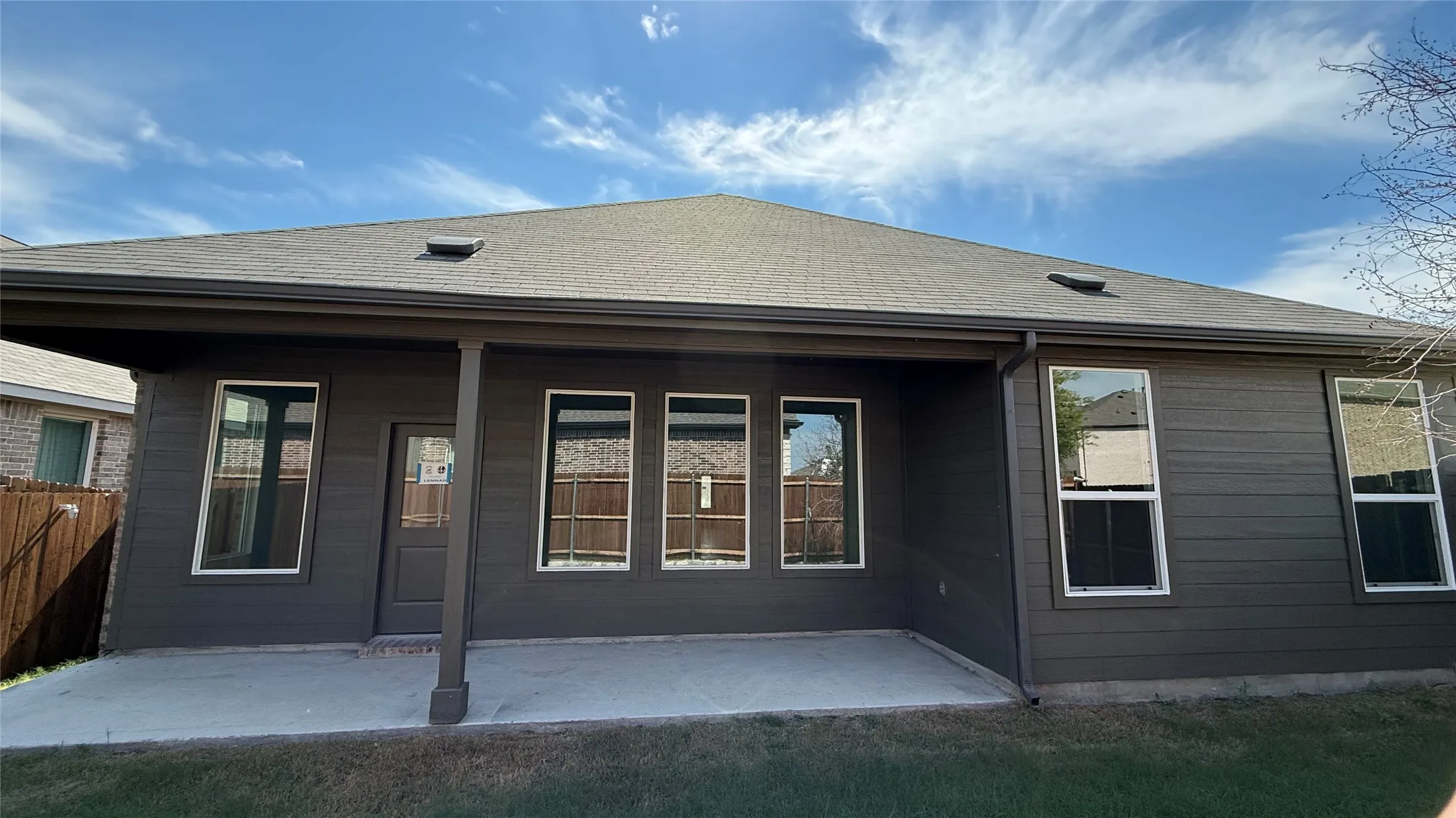 Rear exterior with a covered patio, dark siding, multiple windows, and a dark shingle roof