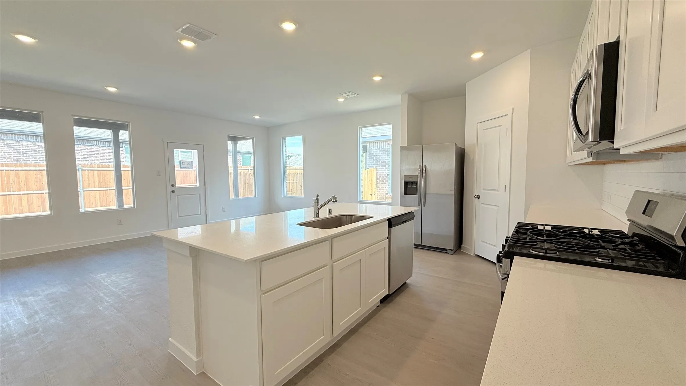 Kitchen island with an undermount sink, white cabinetry, stainless steel appliances, and wood-finish flooring