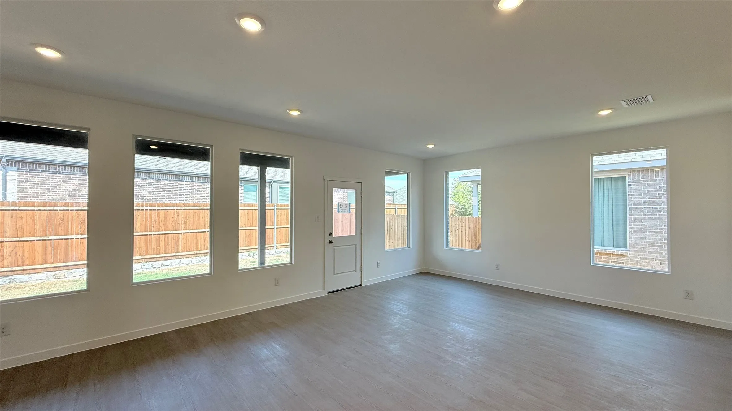 Recessed ceiling lighting, wood-finish flooring, white walls, multiple windows, and a rear exterior door