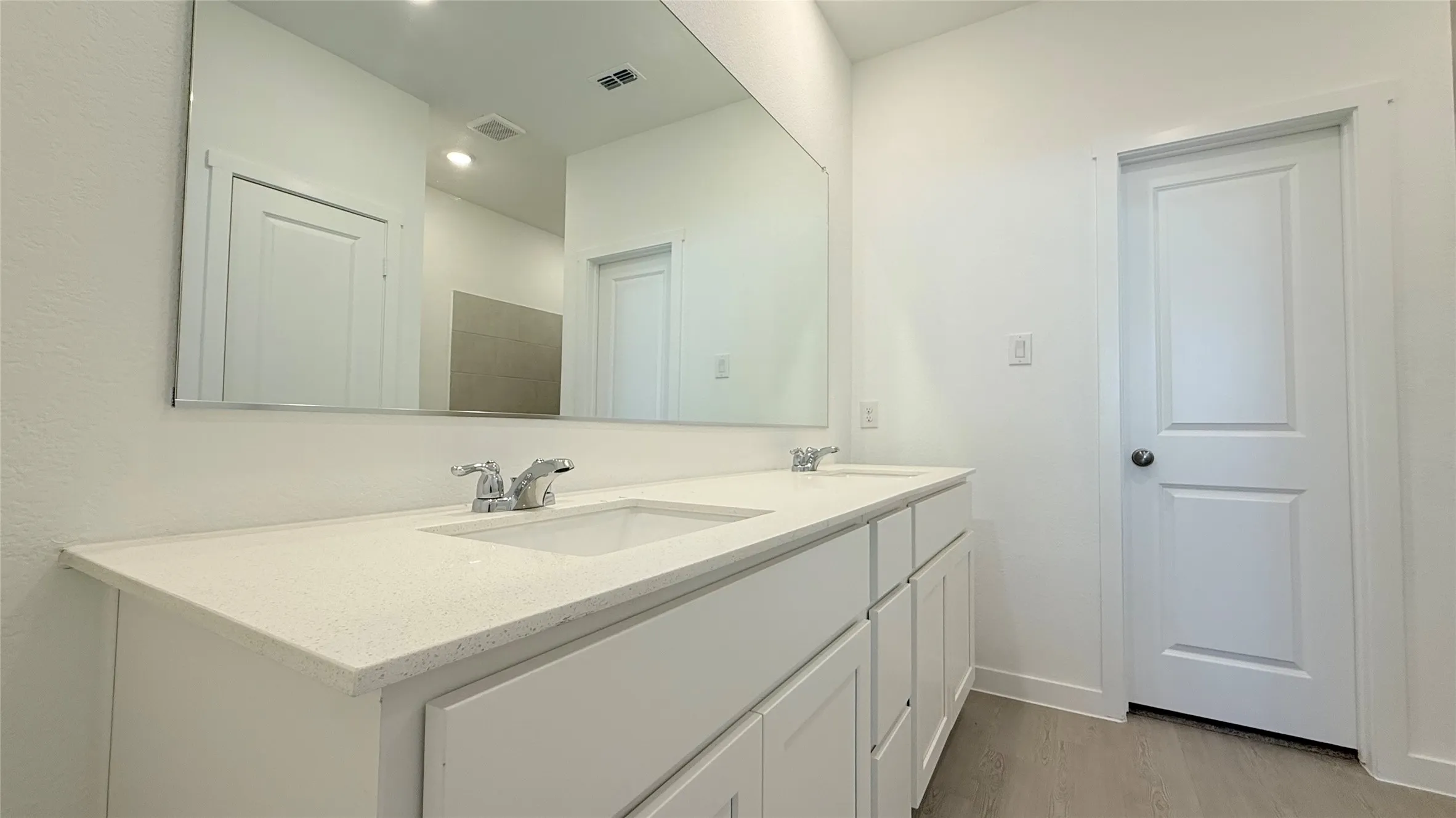 Double vanity with integrated sinks, white cabinetry, chrome fixtures, and a large wall-mounted mirror