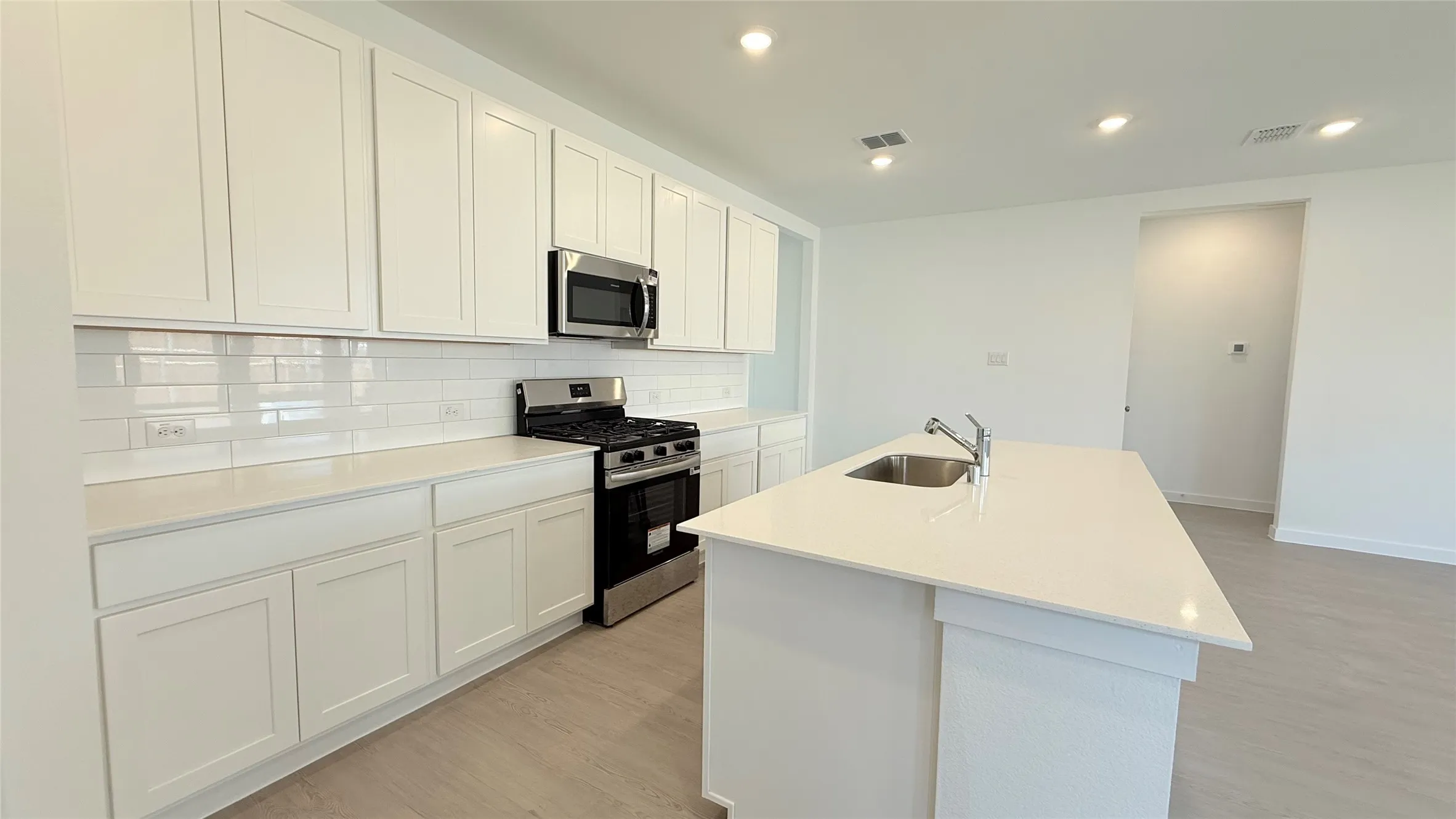 Modern kitchen featuring white shaker cabinetry, white subway tile backsplash, stainless steel appliances, a center island with an undermount sink, and recessed lighting