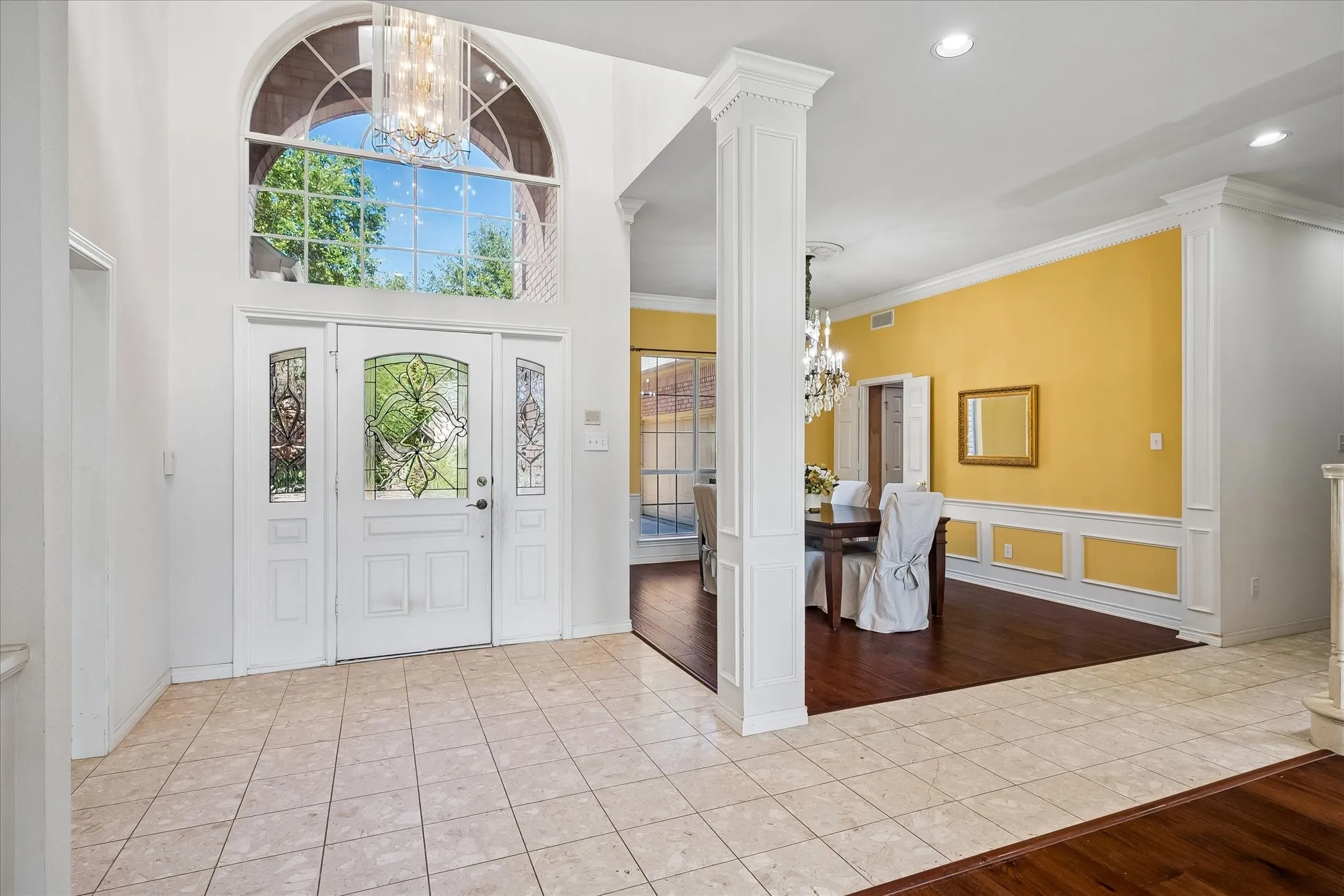 Grand entryway featuring a white double door with leaded glass panels, an arched transom window, and a decorative chandelier