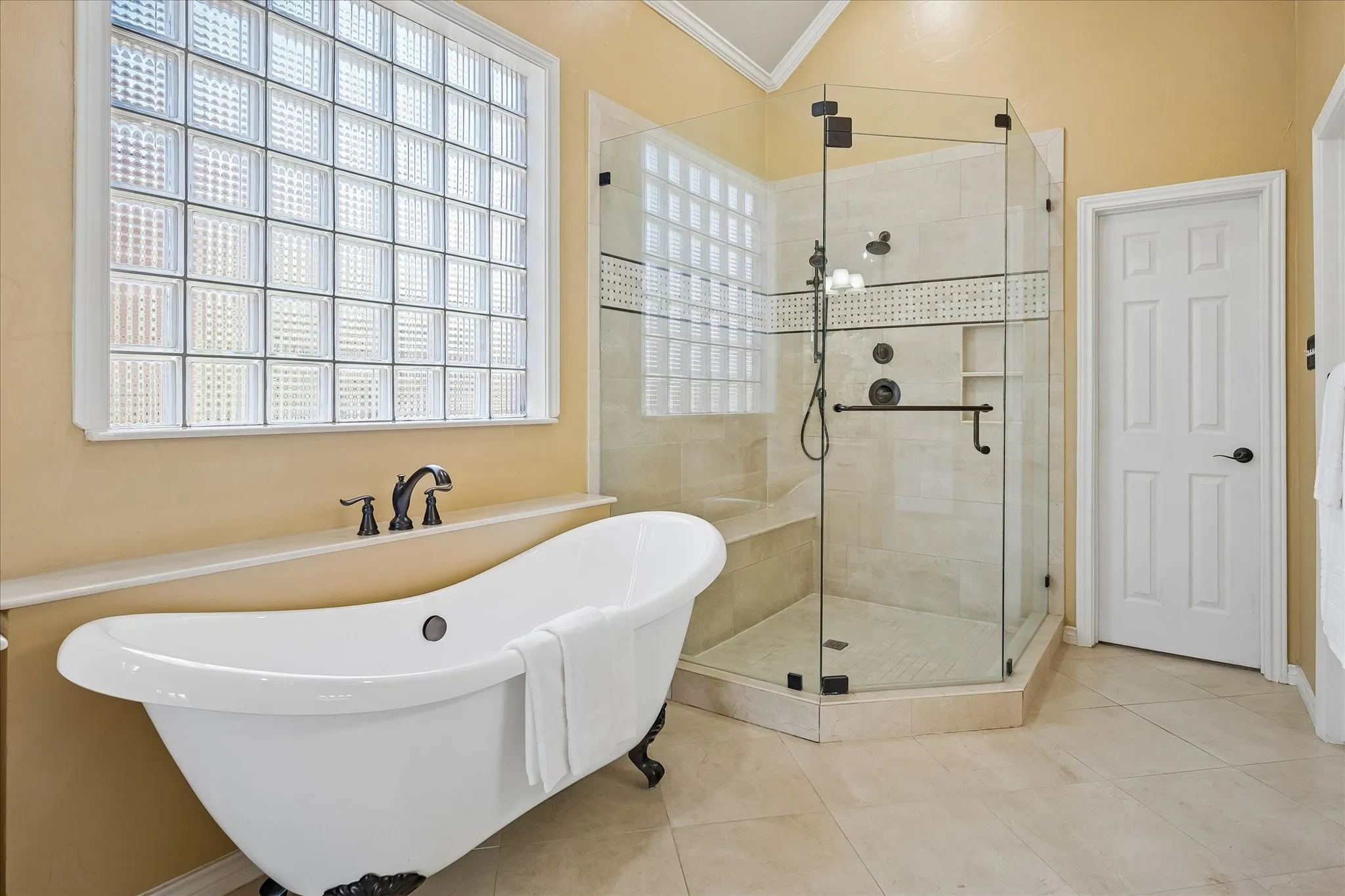 Freestanding soaking tub with bronze fixtures and feet, glass block window, and a frameless glass-enclosed shower with a built-in bench. Two large walk in closets for plenty of storage!