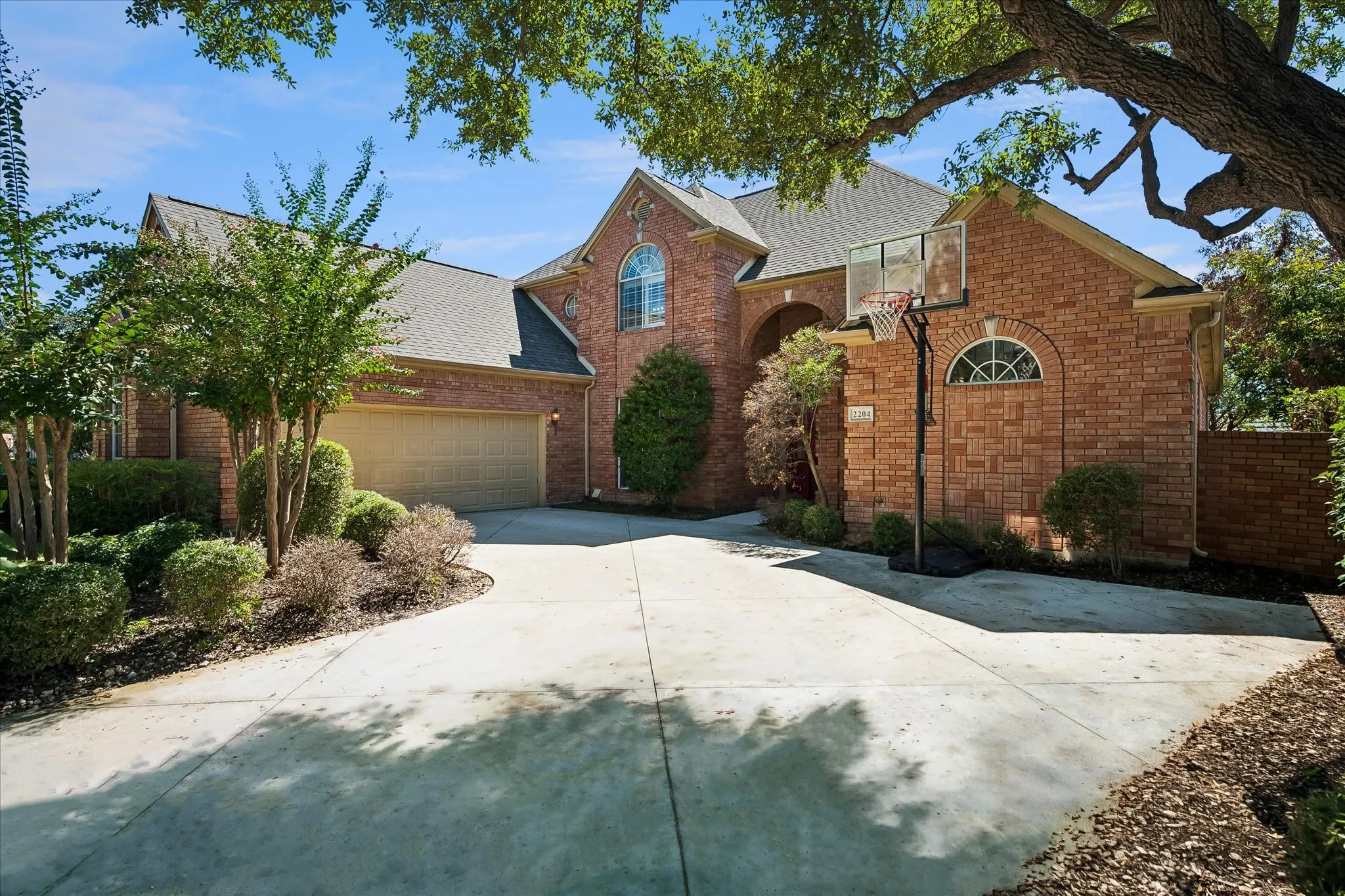 Brick exterior with arched window details, an attached oversized 2 car garage, and a spacious concrete driveway