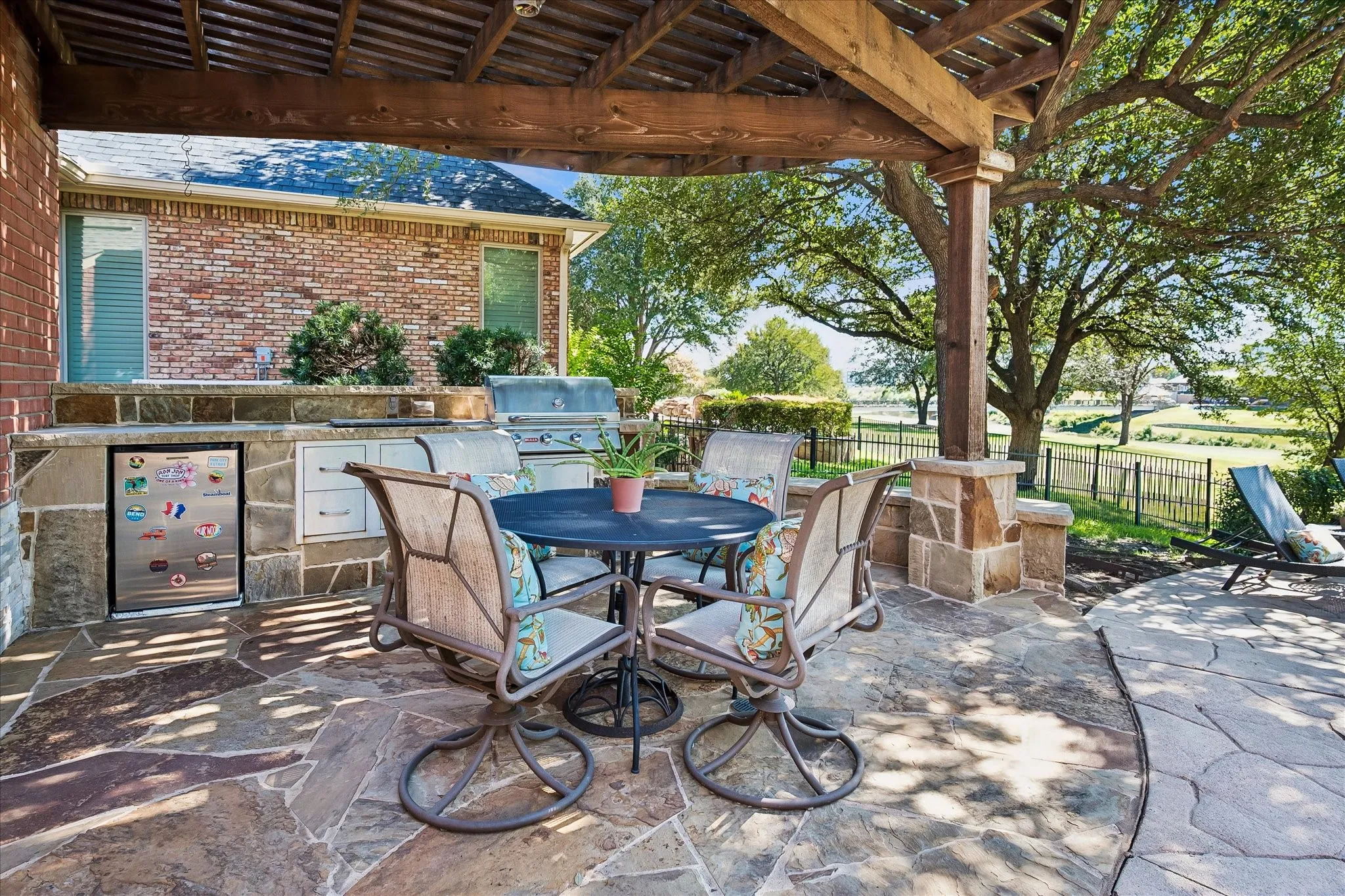 Outdoor patio featuring flagstone flooring, a built-in outdoor kitchen with a grill, refrigerator, storage drawers, and a wood pergola