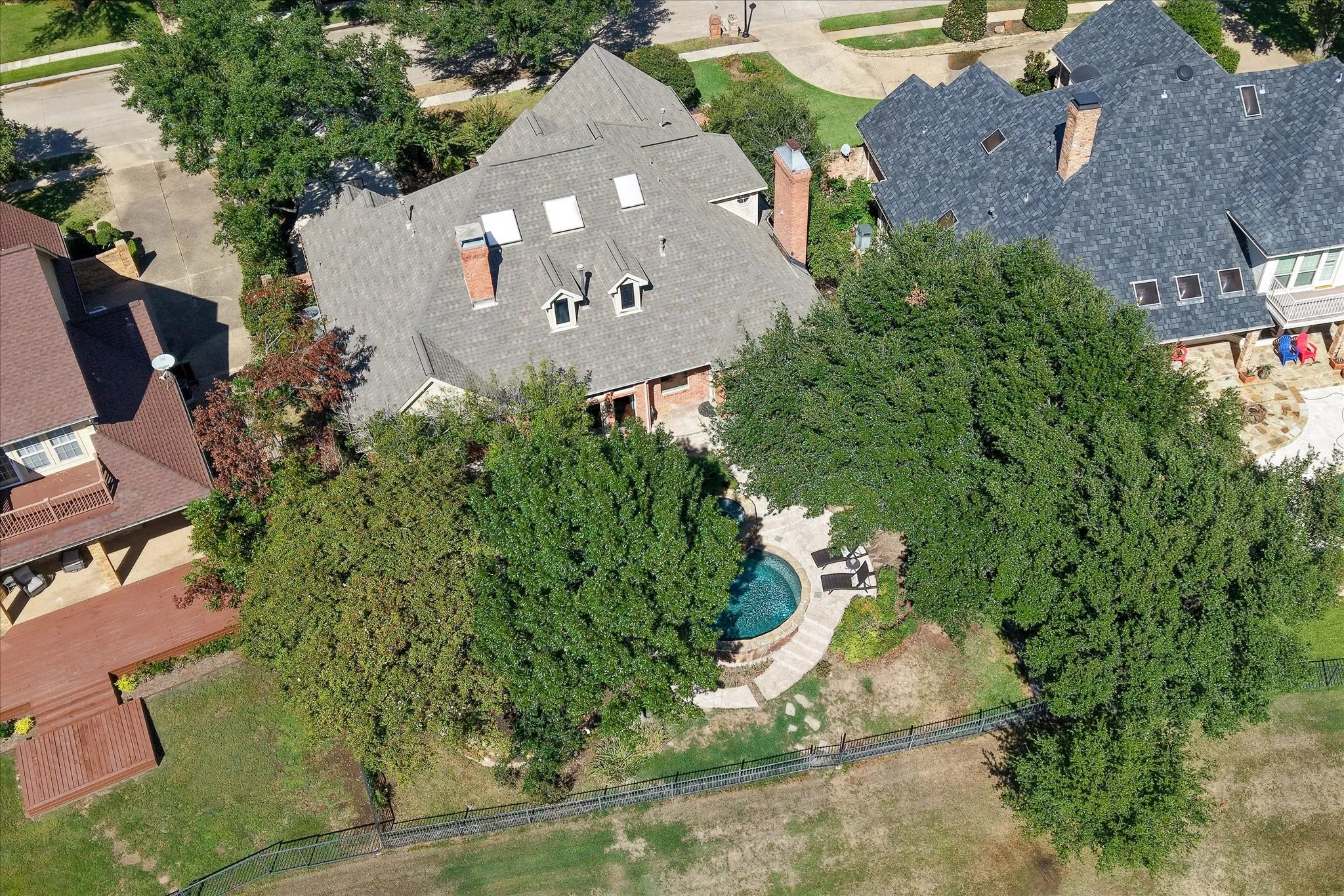 Exterior with a multi-gabled roofline, multiple dormer windows, and skylights amongst mature trees for plenty of shade from the Texas sun!