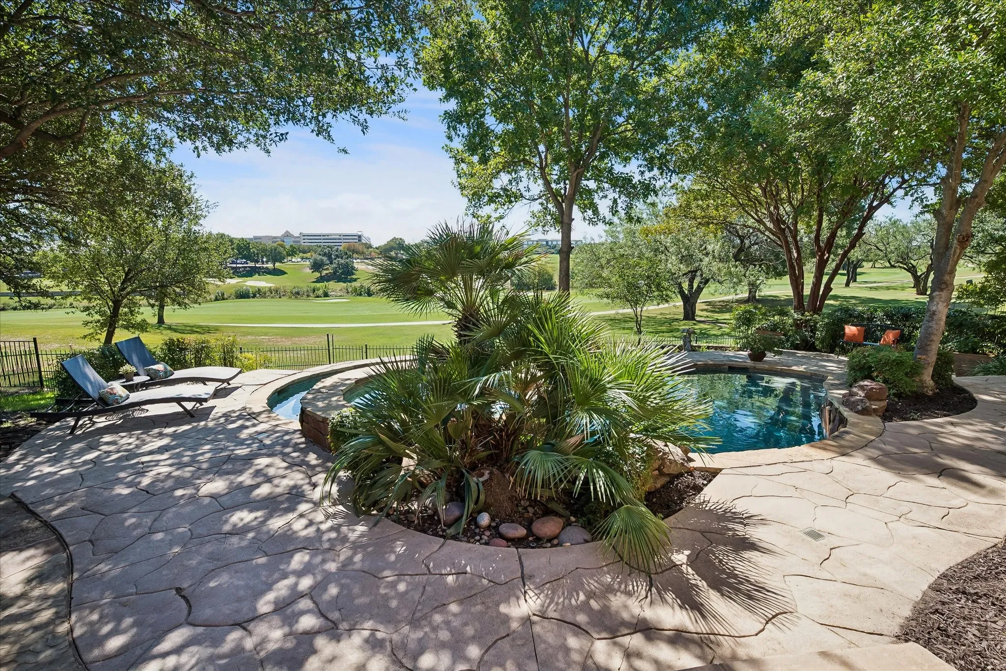 Terraced flagstone patio with a built-in swimming pool and integrated spa, surrounded by mature trees and lush landscaping