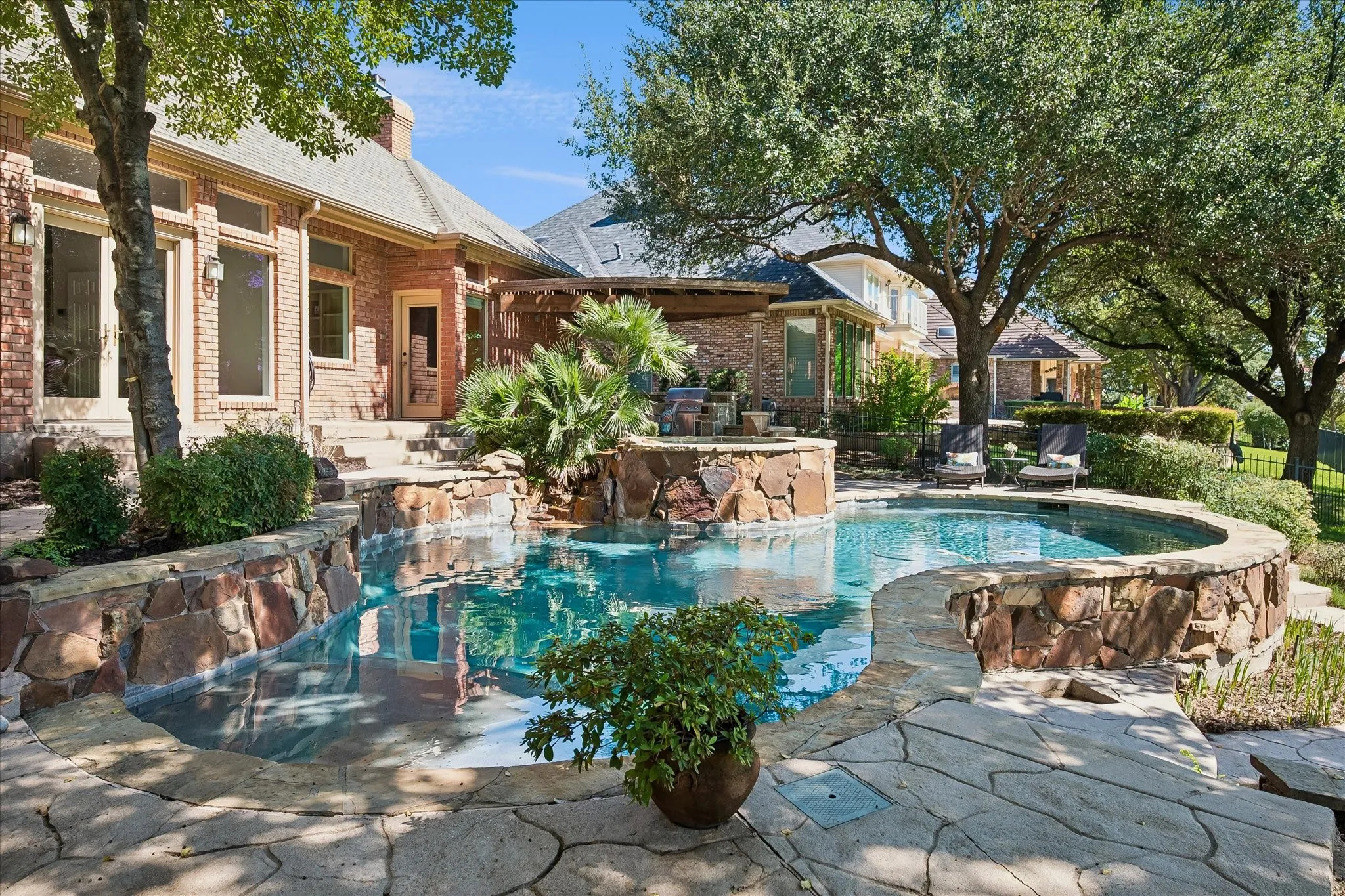 Curved swimming pool with a natural stone surround, flagstone patio, and mature trees