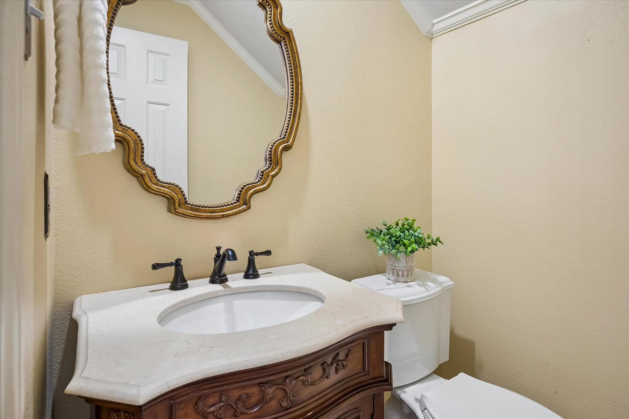Ornate framed mirror over a custom cut marble vanity with an integrated sink and bronze fixtures