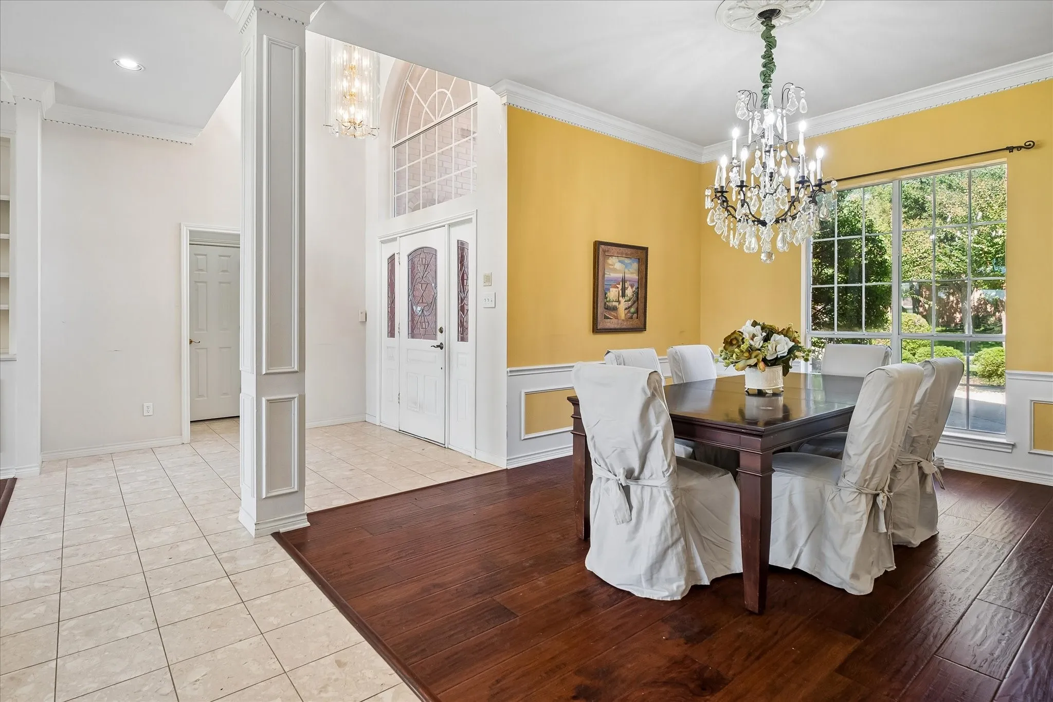 Formal dining space with American Hickory Hardwood, a crystal chandelier, and large window