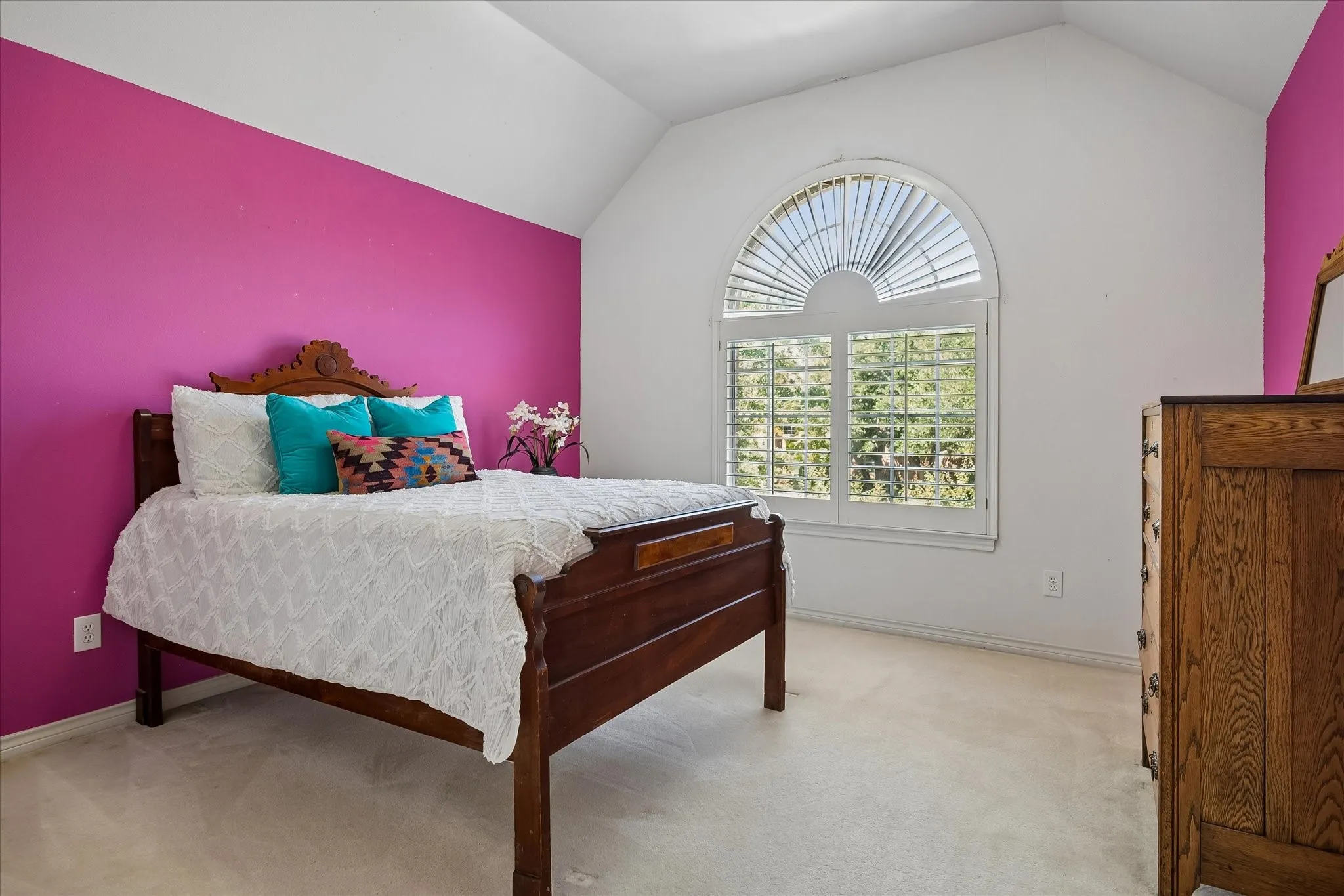 Guest bedroom with arched window with plantation shutters, vaulted ceiling, and carpeted flooring with en suite bath