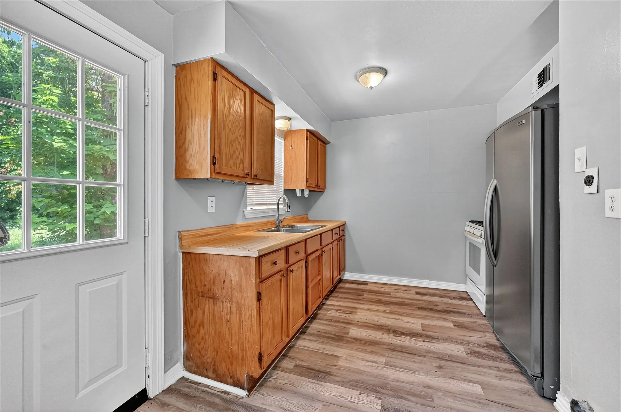Kitchen with freestanding refrigerator, light countertops, light wood-style flooring, brown cabinets, and white stove