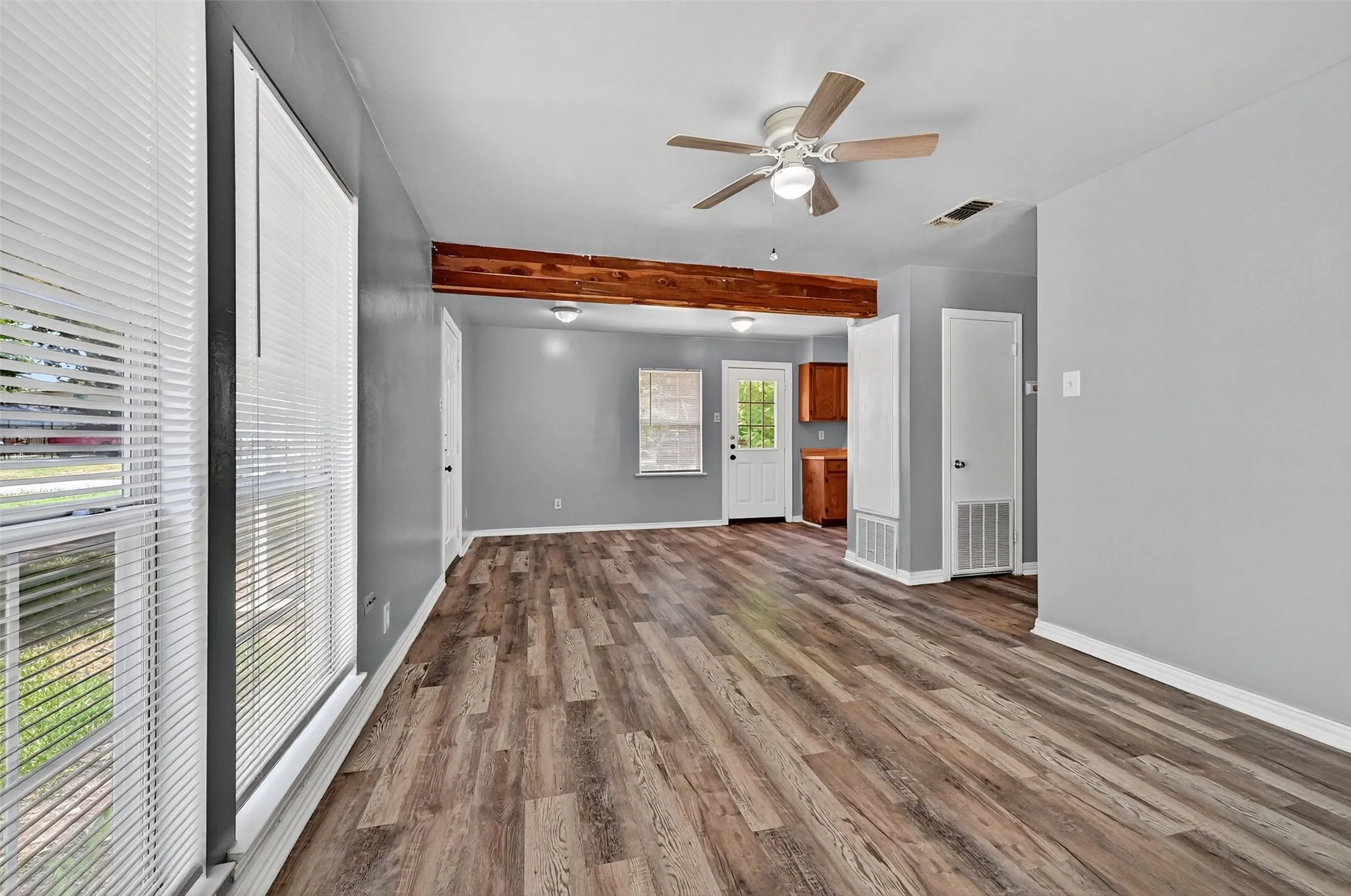 Unfurnished living room with beam ceiling, ceiling fan, and dark wood-style floors