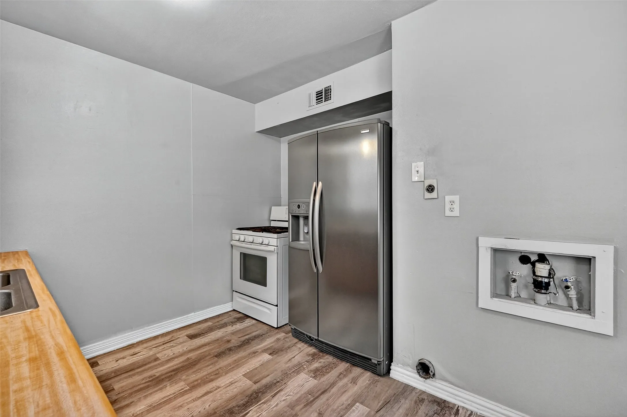 Kitchen with stainless steel fridge, white gas range, wood finished floors, and butcher block countertops