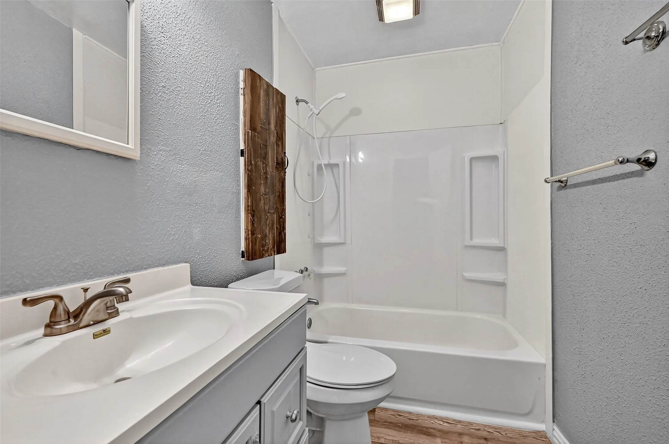 Bathroom with a textured wall, wood finished floors, vanity, and bathing tub / shower combination