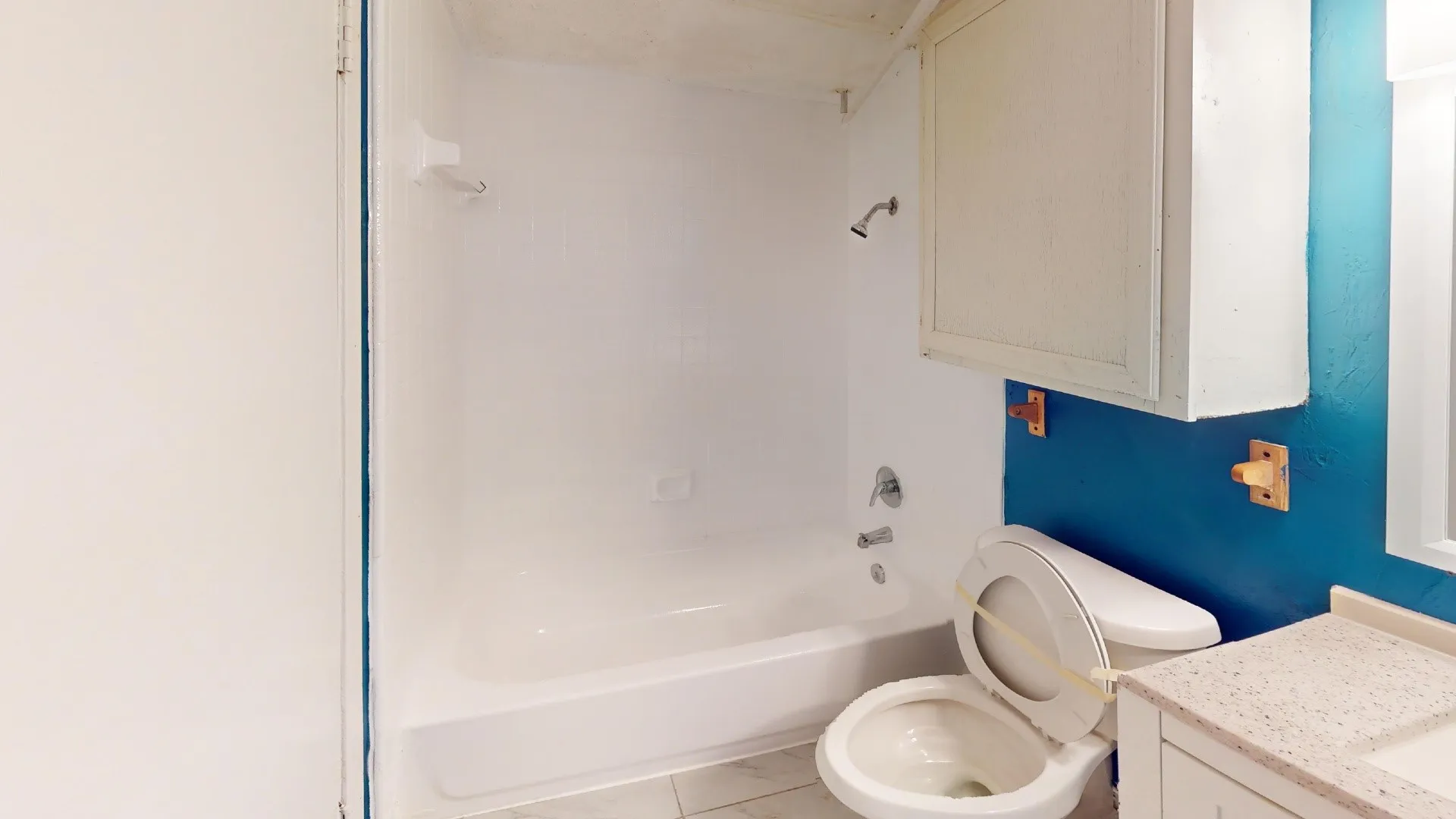 White bathtub with integrated shower, white toilet, and a white vanity with a speckled countertop