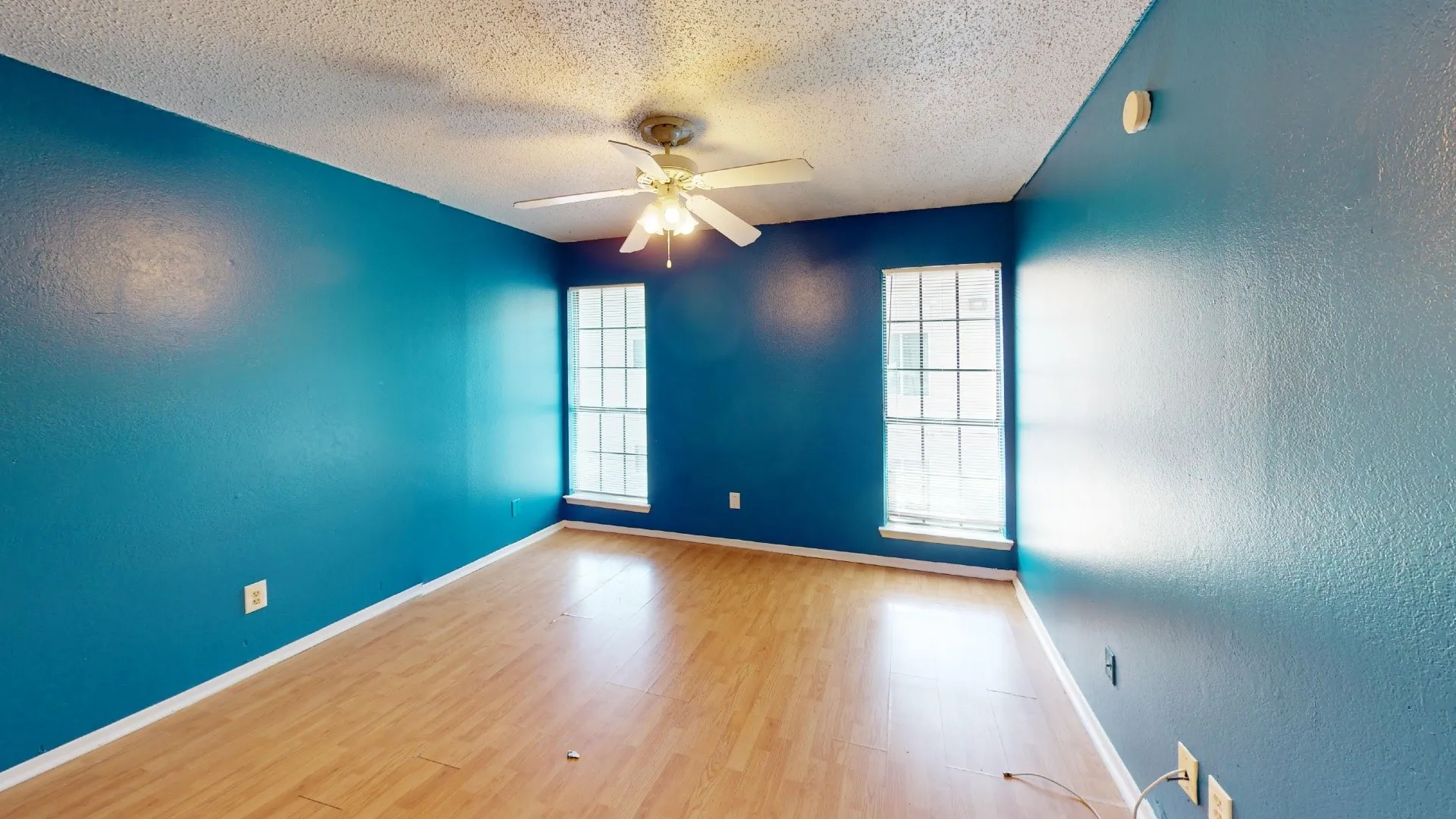 Room featuring wood-finish flooring, two large windows, and a ceiling fan with integrated lighting