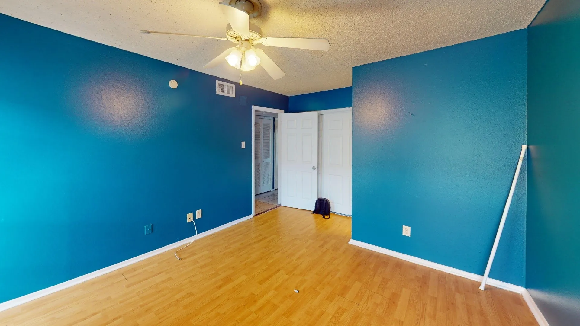 Wood-finish flooring, ceiling fan with integrated lighting, and a white interior door