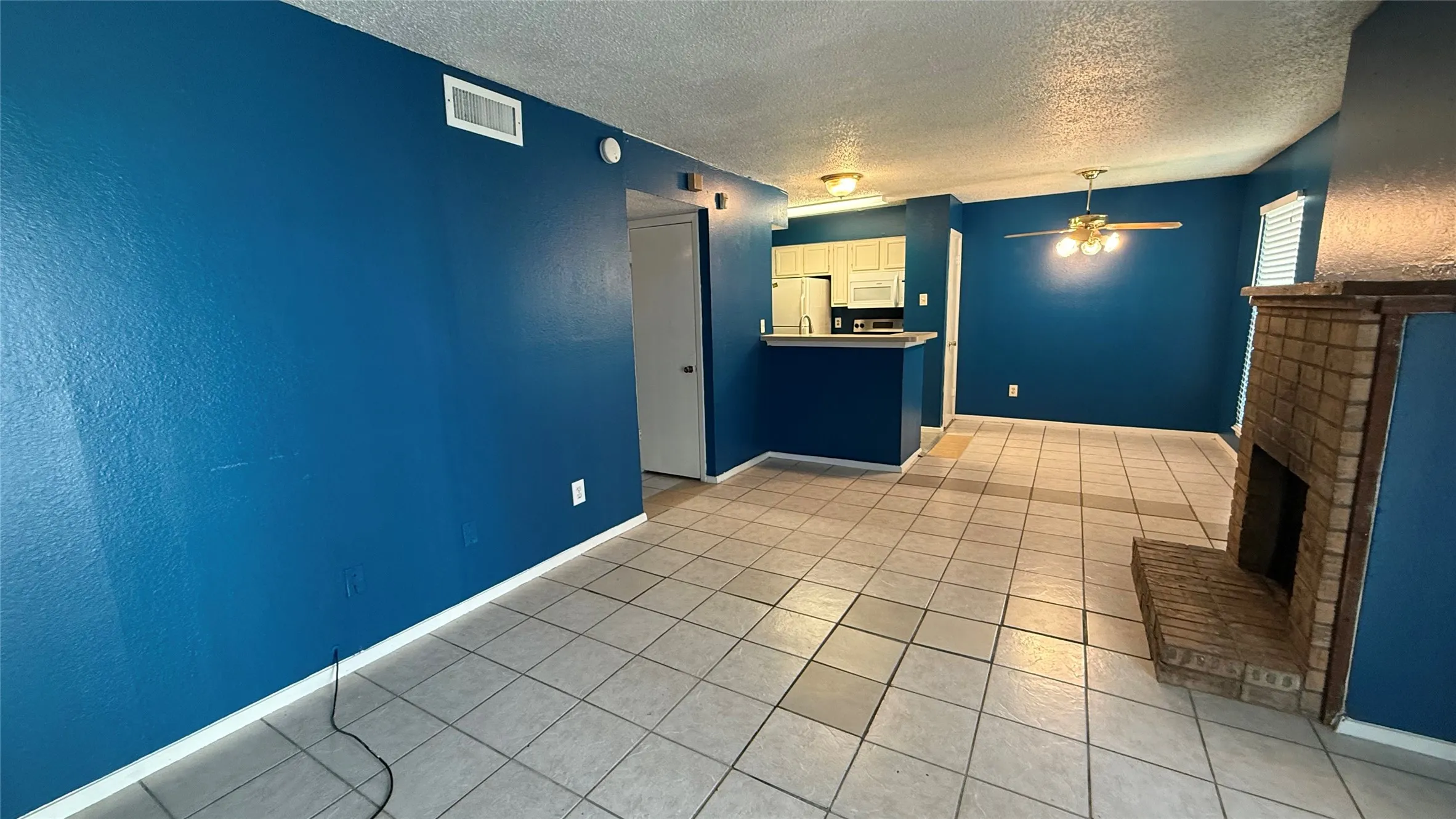 Tile flooring, brick fireplace, built-in breakfast bar, ceiling fan, and white cabinetry